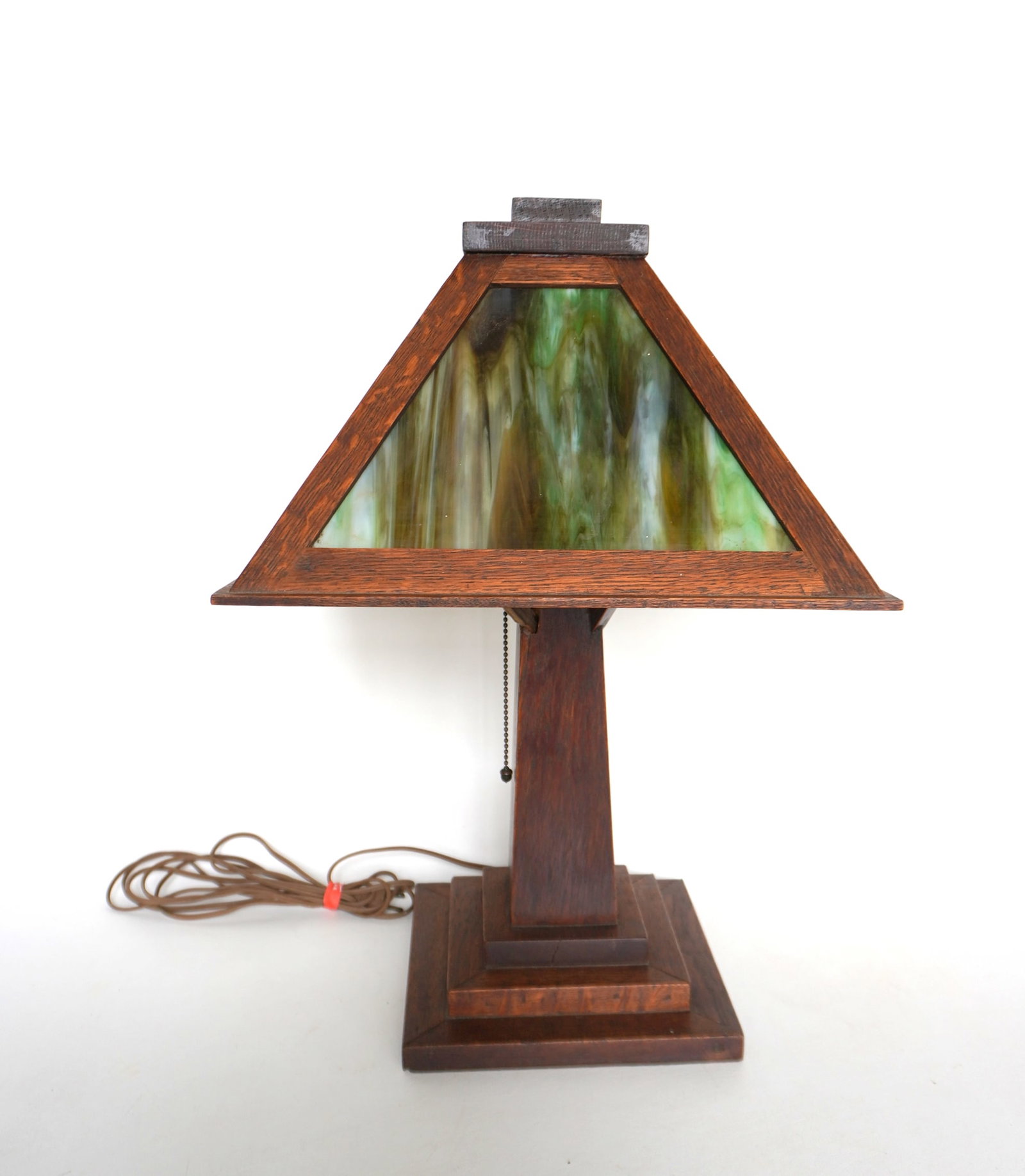 An Arts & Crafts oak slag glass table lamp with 4 green slag glass panels, and having a stepped: An Arts & Crafts oak slag glass table lamp with 4 green slag glass panels, and having a stepped base, circa 1920. One of the 4 arms that hold the shade in place is a replacement, otherwise the lamp is