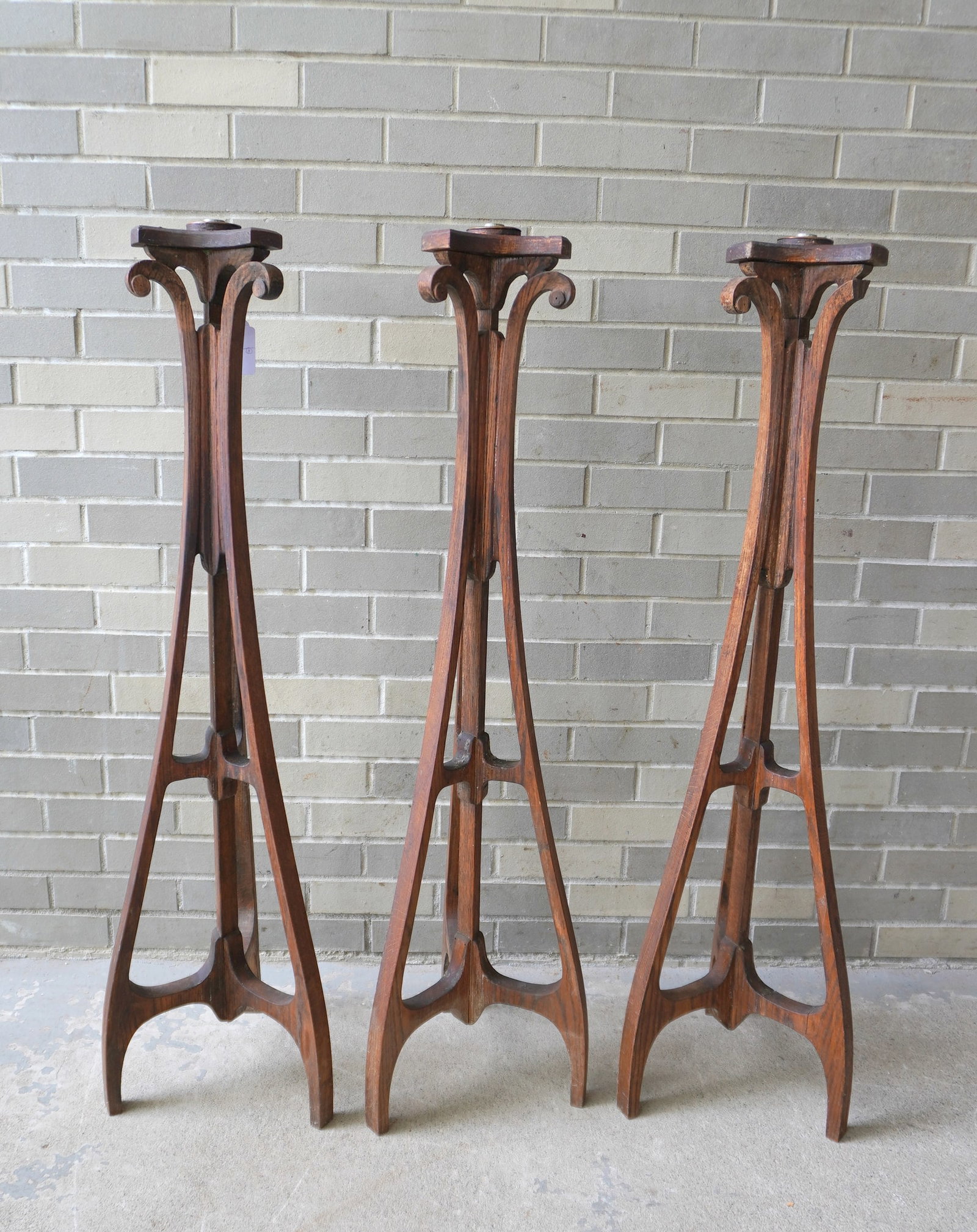 A grouping of 3 matching Masonic Art Nouveau style oak floor standing torchieres each with a single: A grouping of 3 matching Masonic Art Nouveau style oak floor standing torchieres each with a single candle light, late 19th century. Two with a split in one of the lower stretchers, each missing a scr