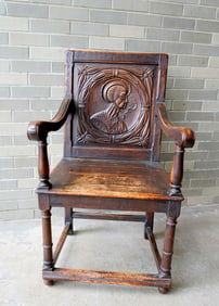 A Jacobean style religious chair with a carved Saint on the back and having rolled arms and turned