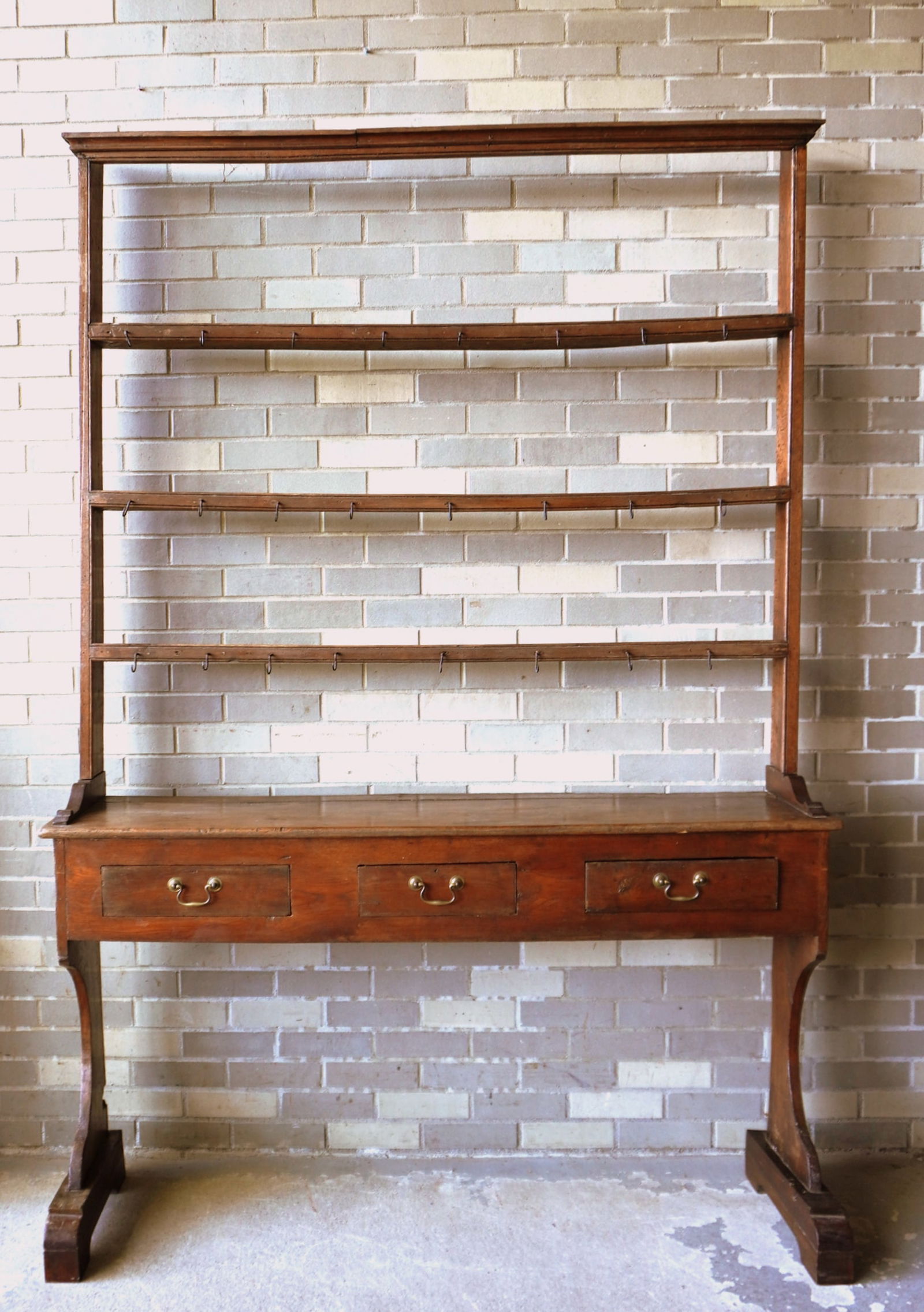 An oak Welsh 2 part cupboard, 18th century. The top section with open front and narrow plate racks: An oak Welsh 2 part cupboard, 18th century. The top section with open front and narrow plate racks has hand forged iron cup hooks applied to the front of each shelf for hanging pewter cups or mugs and