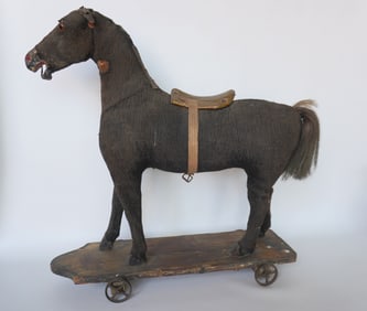 An early horse pull toy having a carved wooden frame, head with glass eyes and body stuffed with