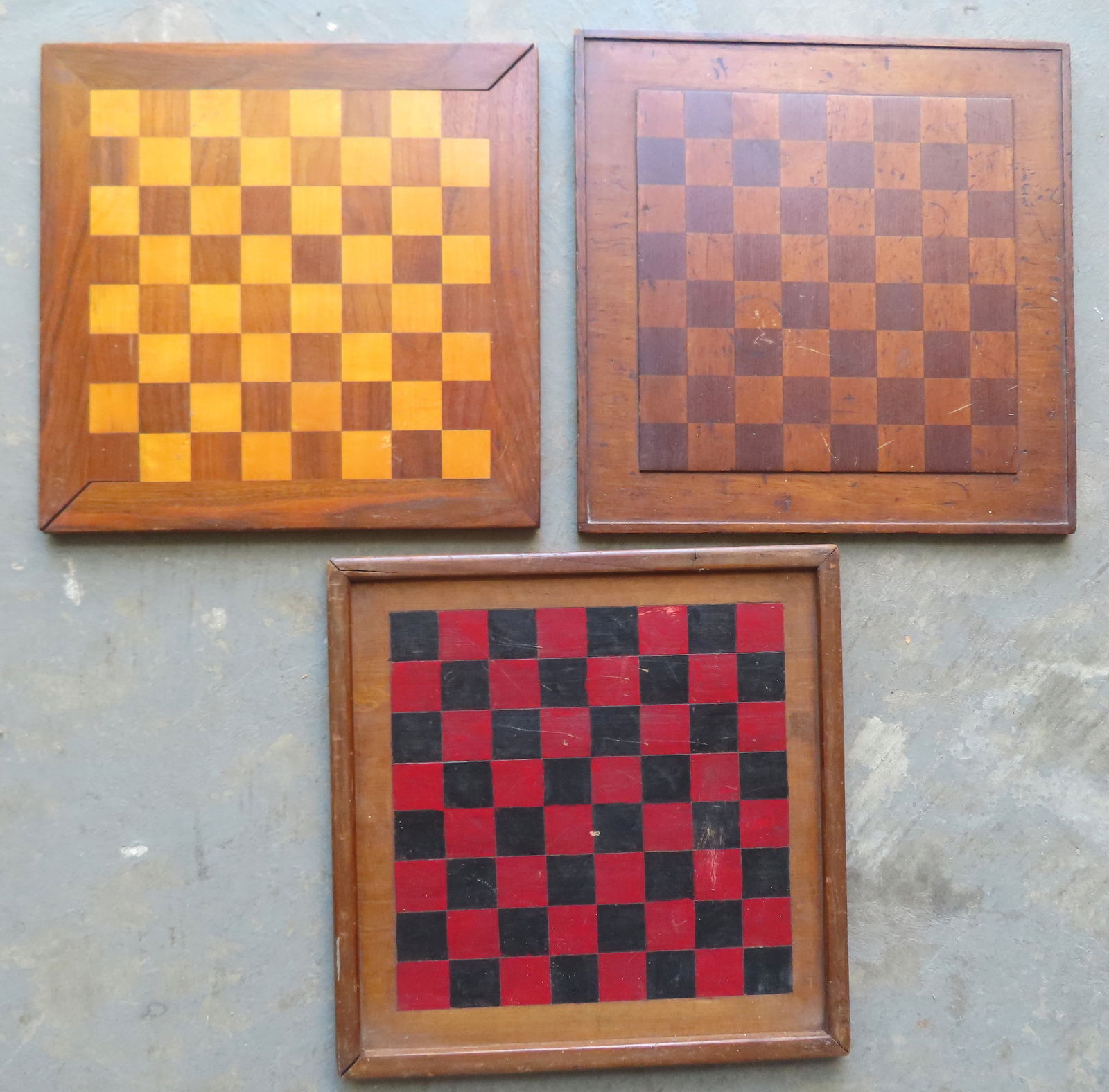 Three gameboards including 2 with inlaid squares in natural wood (one of these double sided), and: Three gameboards including 2 with inlaid squares in natural wood (one of these double sided), and one with hand painted red and black squares. The largest measures 26" square. All in good condition. P