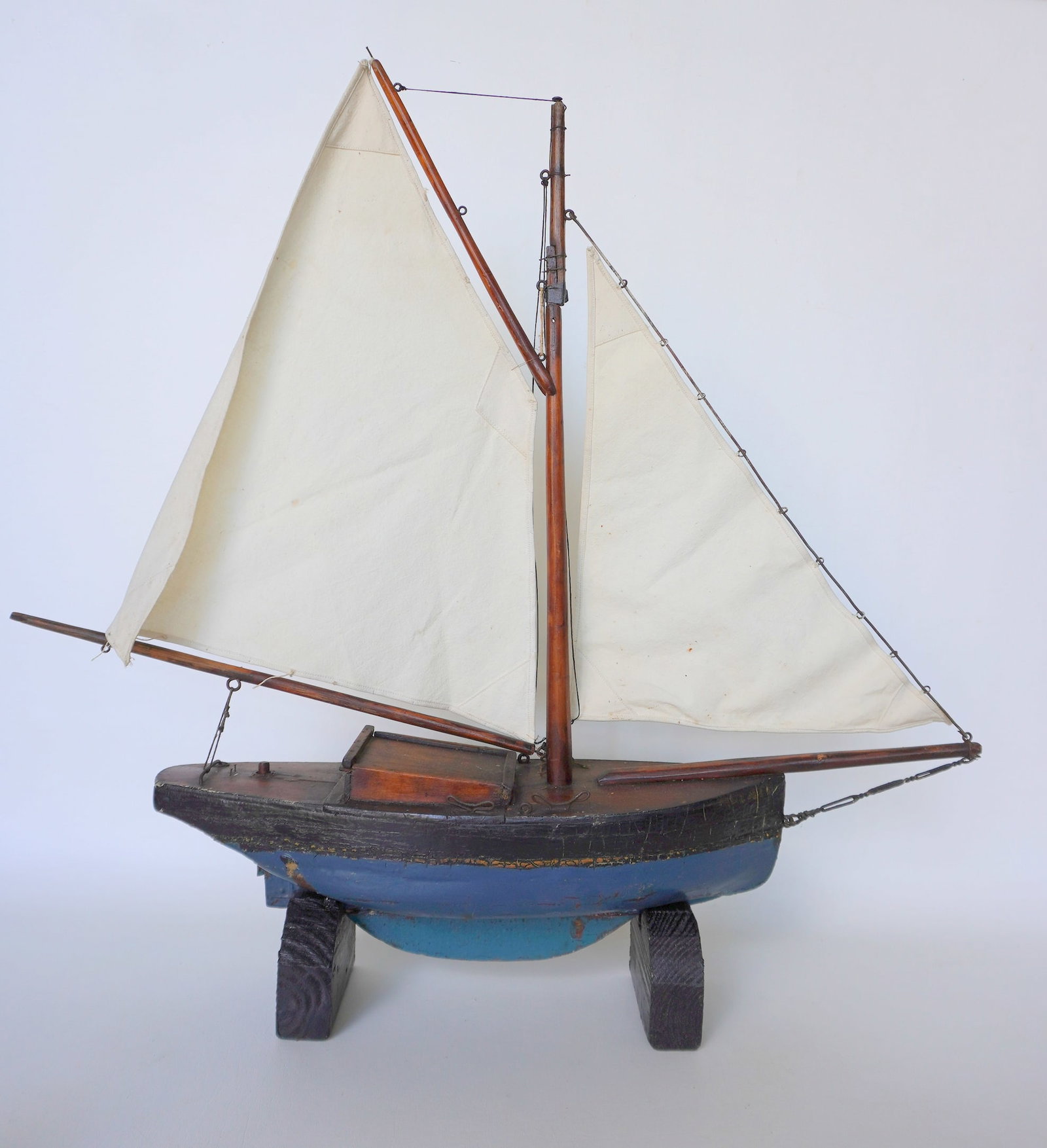 A 19th century hand made wooden sailboat model. The hull in old blue and black paint with some: A 19th century hand made wooden sailboat model. The hull in old blue and black paint with some crazing - the deck with a sliding door that exposes an interior storage compartment - manual working rudd