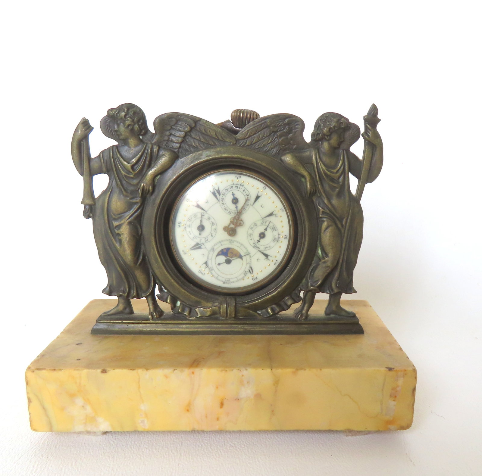 A chronometer pocket watch and an ornate bronze watch holder mounted on marble base. The holder is: A chronometer pocket watch and an ornate bronze watch holder mounted on marble base. The holder is decorated with standing angels holding torchieres - the torch of one angel is missing, the other comp