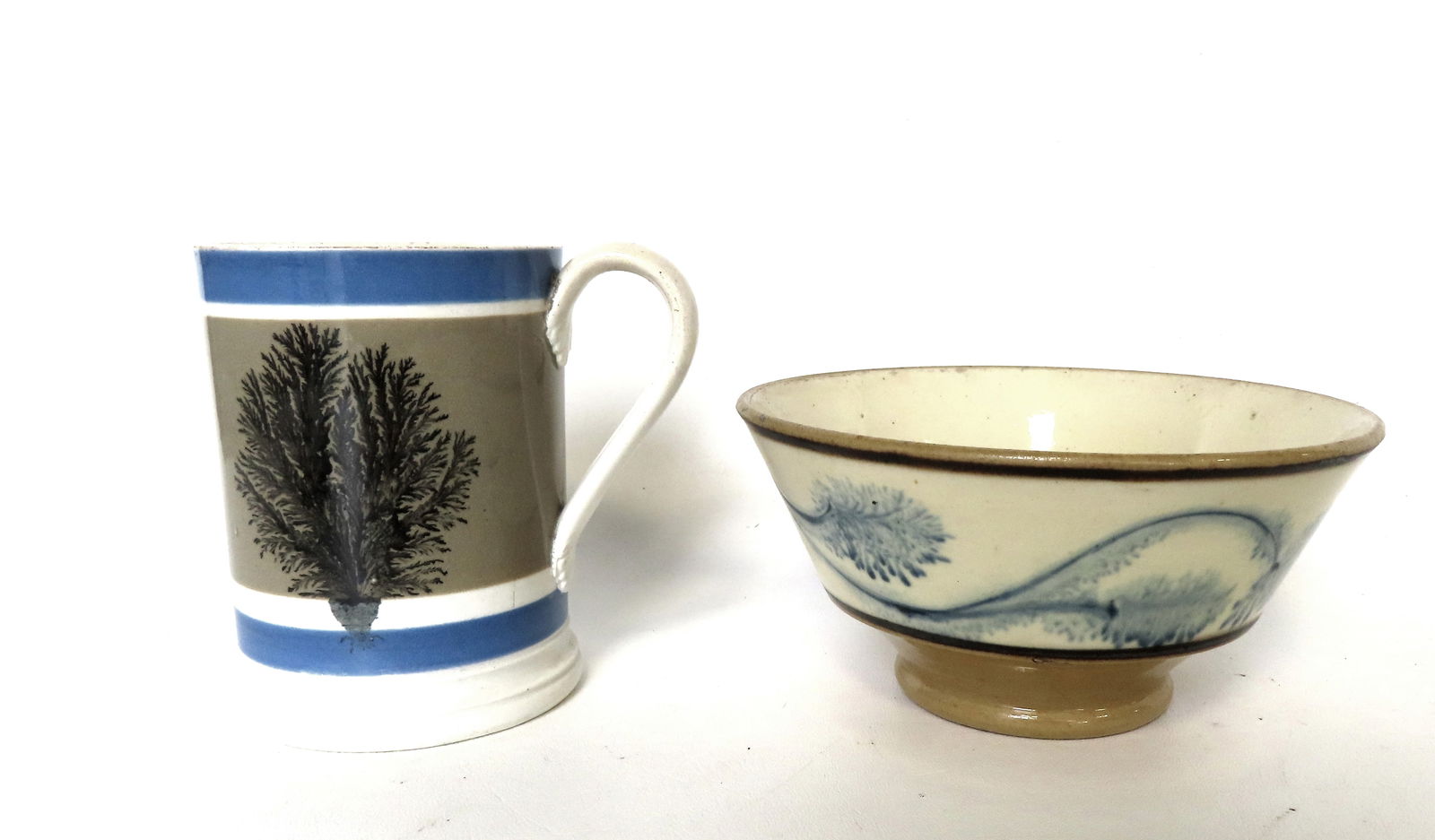 Two pieces of mochaware including cup decorated with tree design - 4 3/4"H; and small bowl decorated: Two pieces of mochaware including cup decorated with tree design - 4 3/4"H; and small bowl decorated with blue seaweed on white ground 6 1/2" diameter x 3 1/4"H. Provenance: From the Marni Bakst and W
