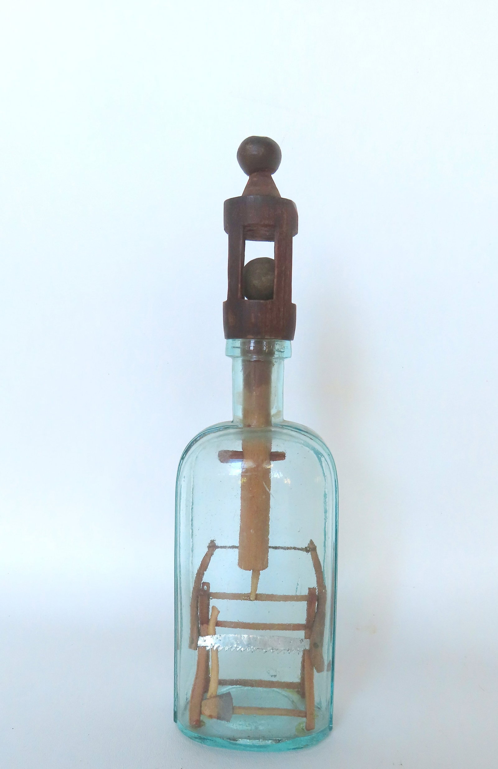 A folk art bottle whimsy with a hand carved stopper carved from 1 piece of wood with loose ball in: A folk art bottle whimsy with a hand carved stopper carved from 1 piece of wood with loose ball in cage design attached to pole that is inserted into bottle to form a lock as it has a horizontal dowel