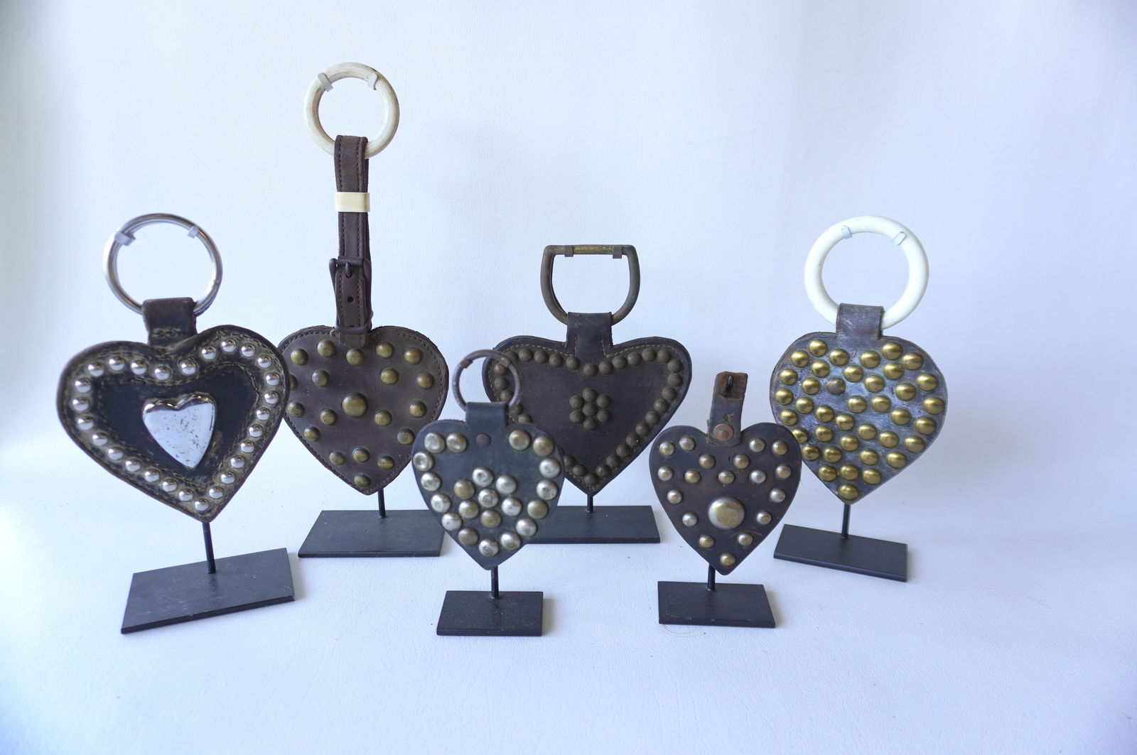 Grouping of 6 leather heart shaped horse harness decorations, all with applied brass and silver: Grouping of 6 leather heart shaped horse harness decorations, all with applied brass and silver buttons conforming to the shape of the ornament - one also with a large nickel plated heart shaped ornam