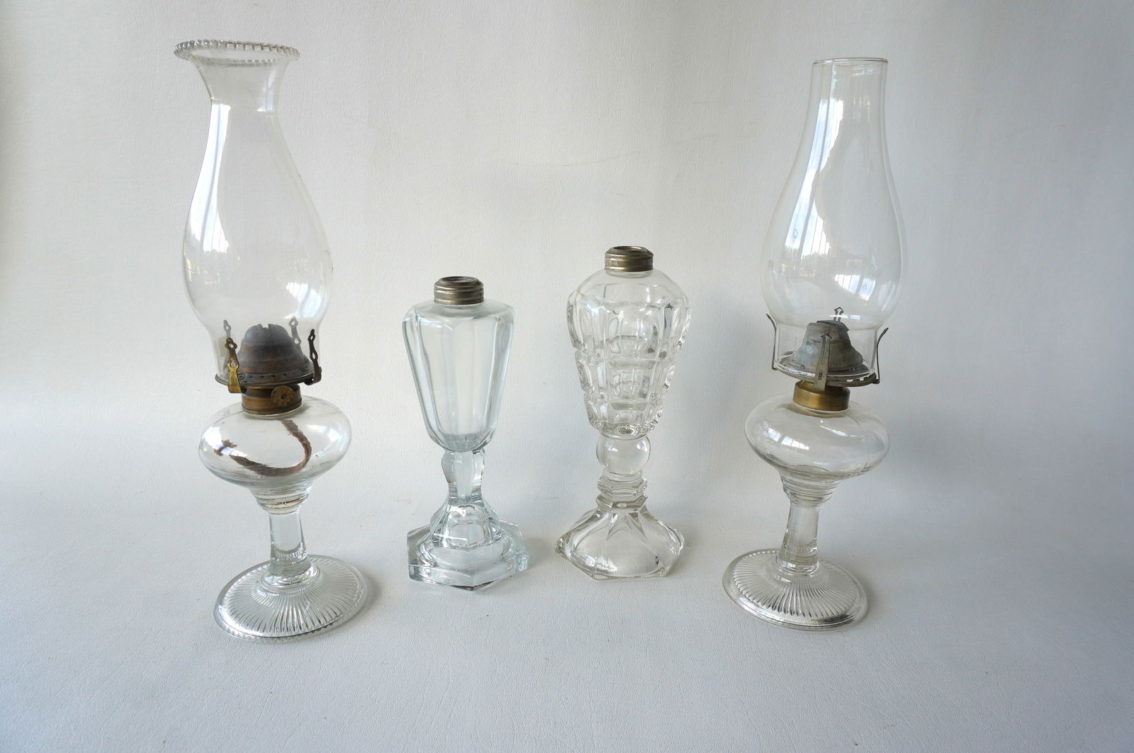 Grouping of 4 glass lighting devices including: 2 whale oil lamps, 19th century - the largest 9: Grouping of 4 glass lighting devices including: 2 whale oil lamps, 19th century - the largest 9 1/2"H; and 2 good matching oil lamps - the base appears to be applied to the font, circa 1860 - both in
