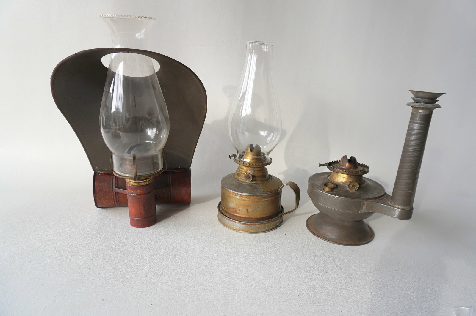 Three unusual lanterns including: The first, the largest, with cylindrical reservoir and tin hood: Three unusual lanterns including: The first, the largest, with cylindrical reservoir and tin hood with attachment for hand use, hanging on wall on standing on cupboard, mid 19th century - 11"H x 6 1/4