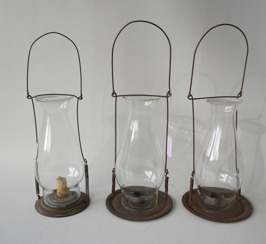 Three hanging wire and tin candle lanterns, early to mid 18th century. All in good condition with: Three hanging wire and tin candle lanterns, early to mid 18th century. All in good condition with chimneys - each measures approximately 13 1/2"H x 4 1/2" diameter at base. Provenance: From the Marni