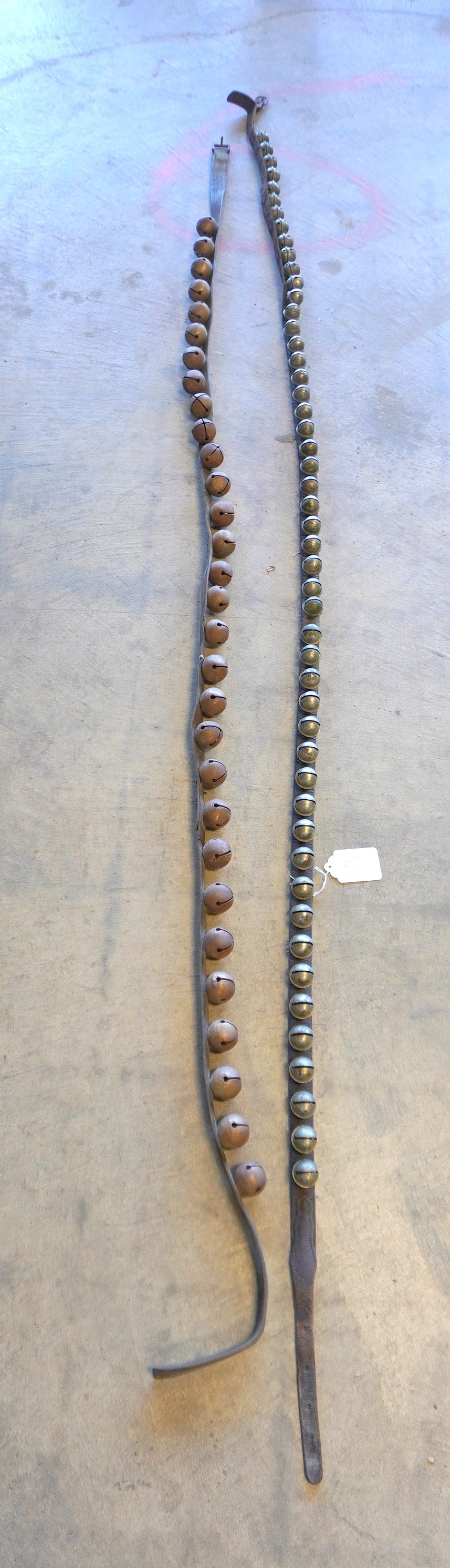 Two complete sets of circular brass sleigh bells attached to original leather straps and retaining: Two complete sets of circular brass sleigh bells attached to original leather straps and retaining original buckles. The first set with 50 bells and having an overall length of 92" - the leather worn