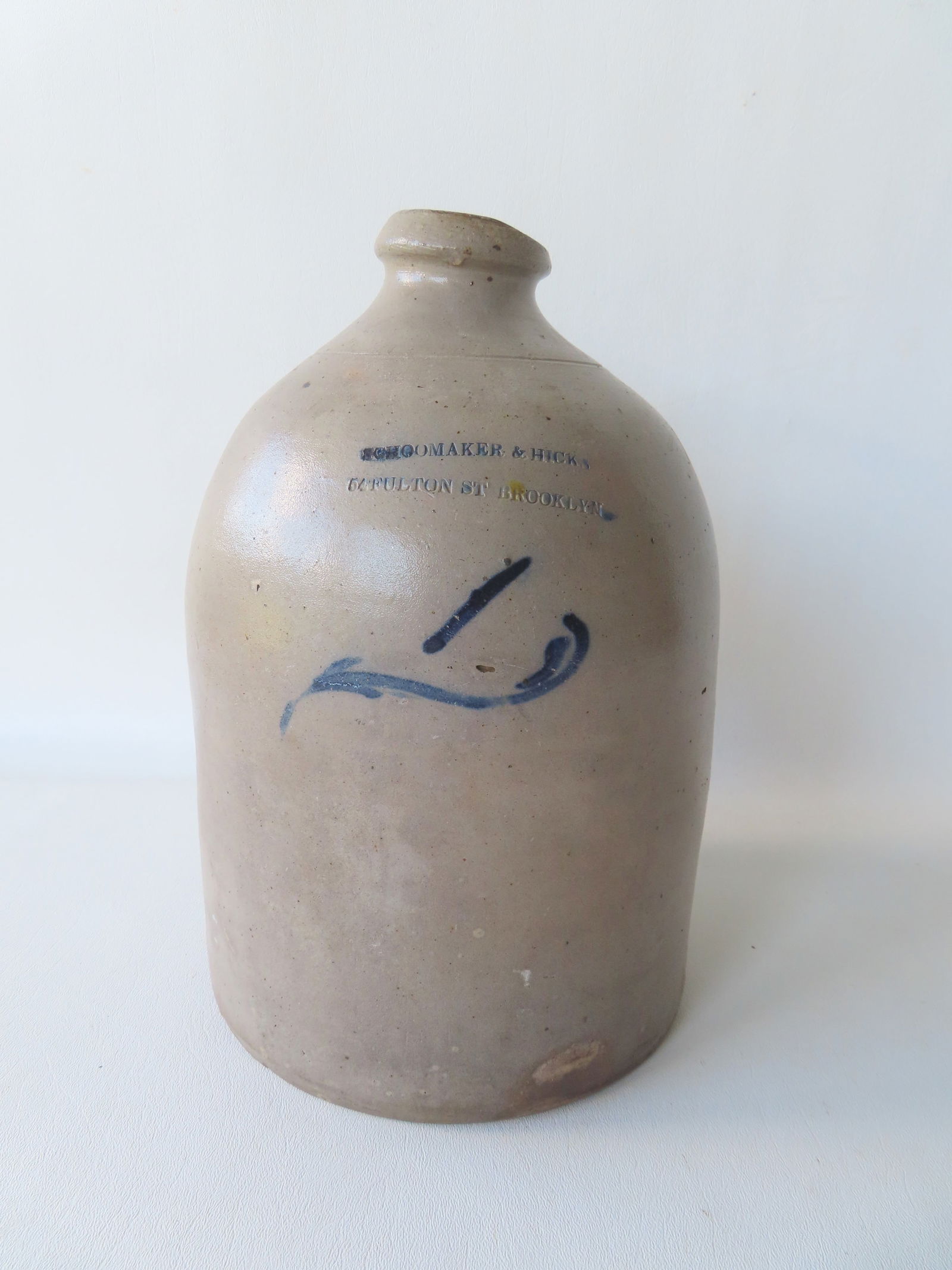 Stoneware advertising jug with the impressed mark of "SCHOOMAKER & HICKS / 54 FULTON ST. BROOKLYN": Stoneware advertising jug with the impressed mark of "SCHOOMAKER & HICKS / 54 FULTON ST. BROOKLYN" (Should be Schoonmaker) and decorated with a cobalt blue "1" of vine mark - there appears to be chip