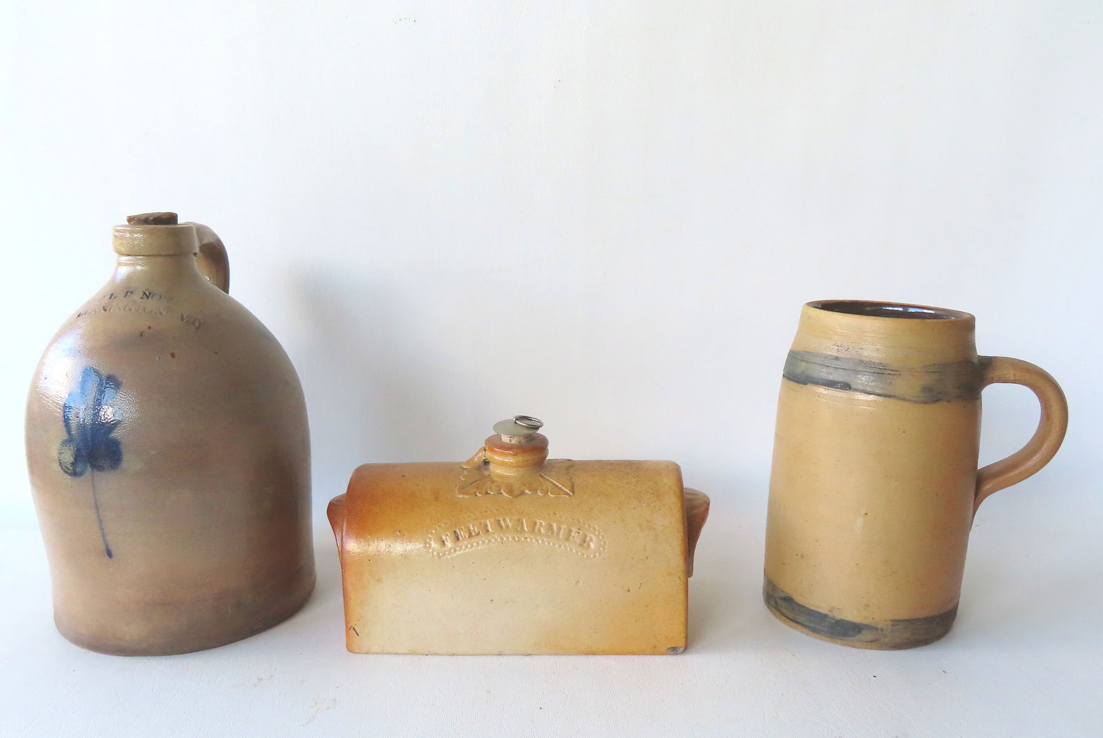 Three pieces of stoneware including: A signed "FEETWARMER" with fancy handles on ends - very good: Three pieces of stoneware including: A signed "FEETWARMER" with fancy handles on ends - very good condition; pitcher with 2 cobalt blue rings - very good condition; and a jug with the impressed mark o