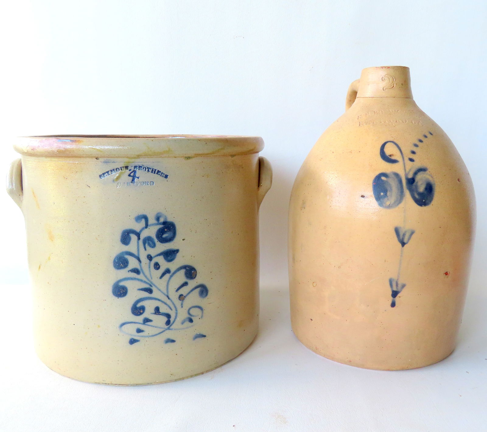 A stoneware crock and jug. The crock, 4 gallon, with the impressed mark of "SEYMOUR BROTHERS /: A stoneware crock and jug. The crock, 4 gallon, with the impressed mark of "SEYMOUR BROTHERS / HARTFORD", and decorated with a cobalt blue flower - measures 10 1/2"H x 12" diameter - 2 professional re