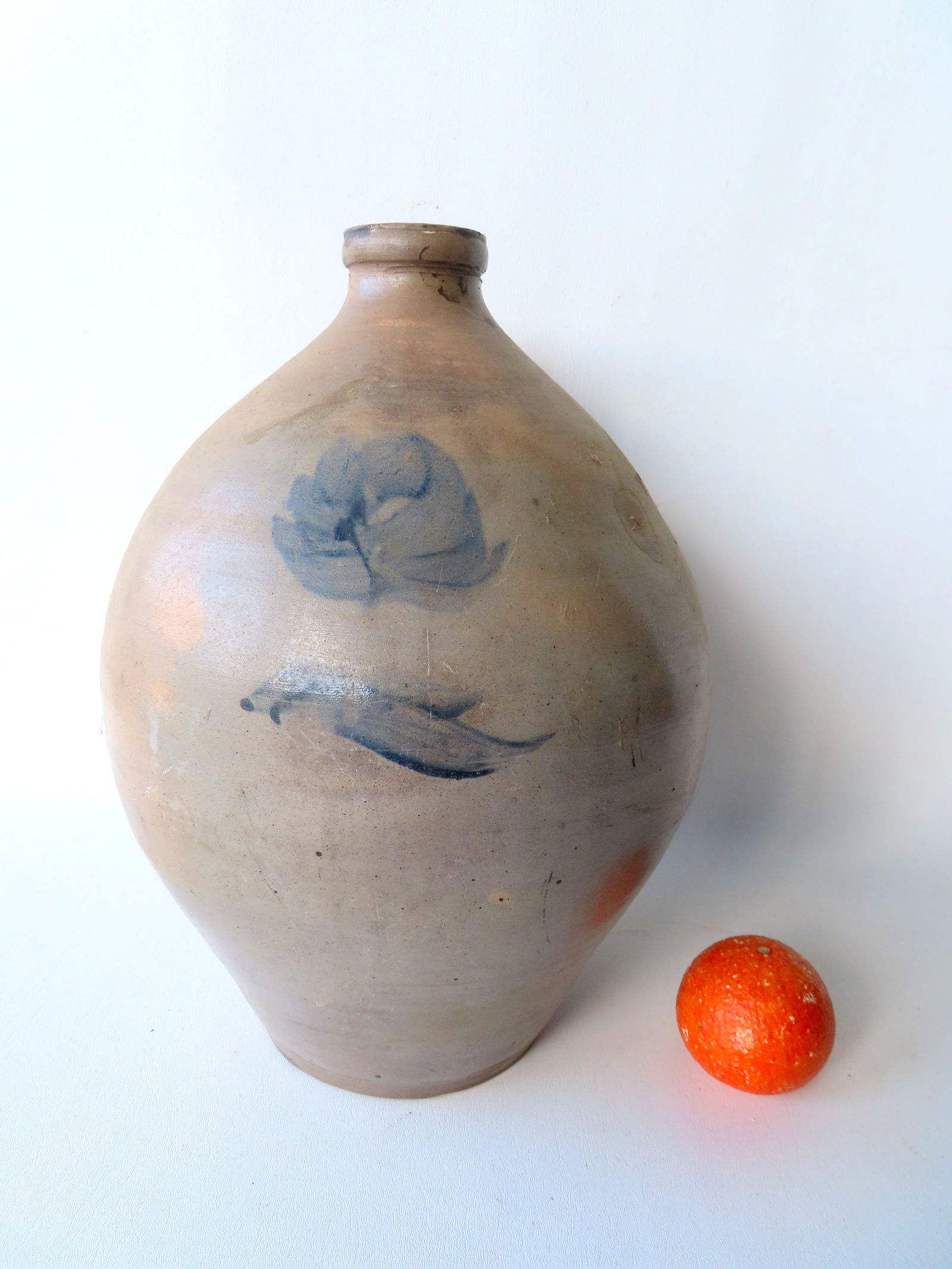 A stoneware ovoid jug, unmarked but either 3 or 4 gallon, decorated with a cobalt blue flower on: A stoneware ovoid jug, unmarked but either 3 or 4 gallon, decorated with a cobalt blue flower on front and cobalt blue on base of handle. The back side of jug with cracks and chips (see photos), else