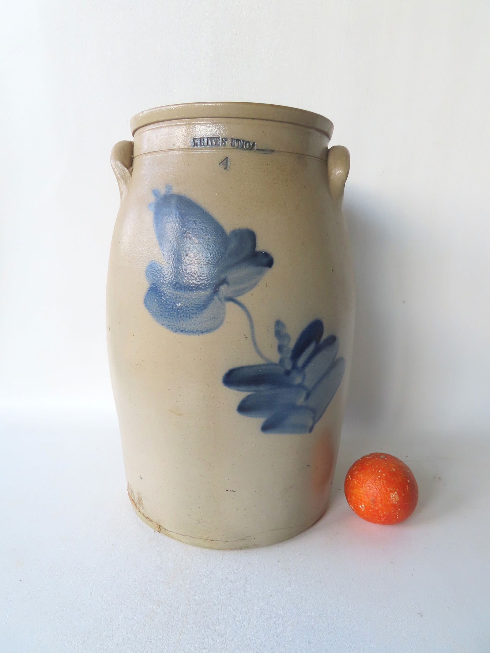 A stoneware butter churn, 4 gallon, with the impressed mark of "WHITE'S UTICA", decorated with a: A stoneware butter churn, 4 gallon, with the impressed mark of "WHITE'S UTICA", decorated with a large cobalt blue flower - repaired crack along edge of base, else good condition. Measures 16 1/4"H x