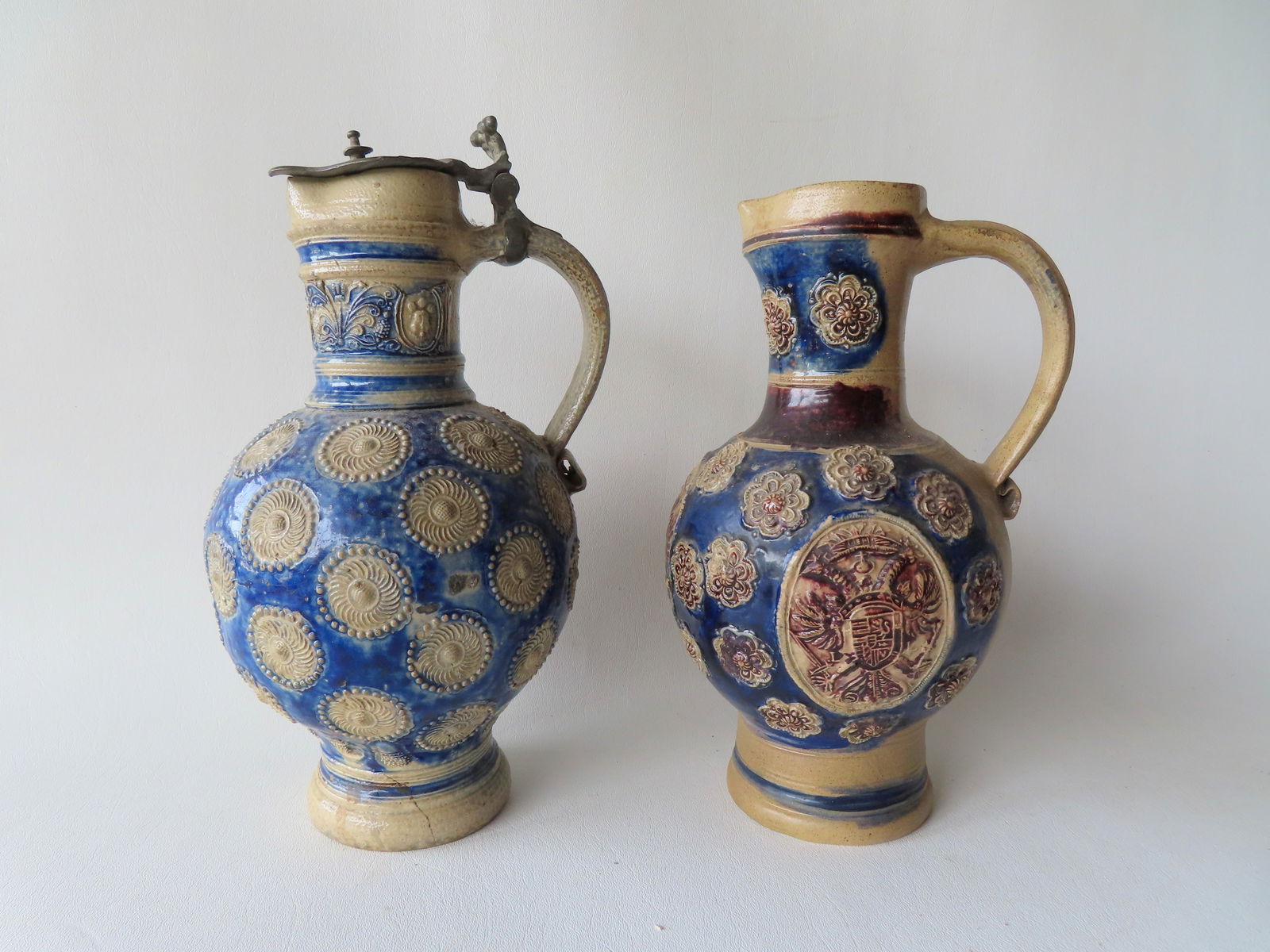 Two Westerwald stoneware jugs, both believed to be 18th century. The first, decorated with raised: Two Westerwald stoneware jugs, both believed to be 18th century. The first, decorated with raised floral medallions on the body and the neck decorated with flowers with scrolled leaves and raised mask