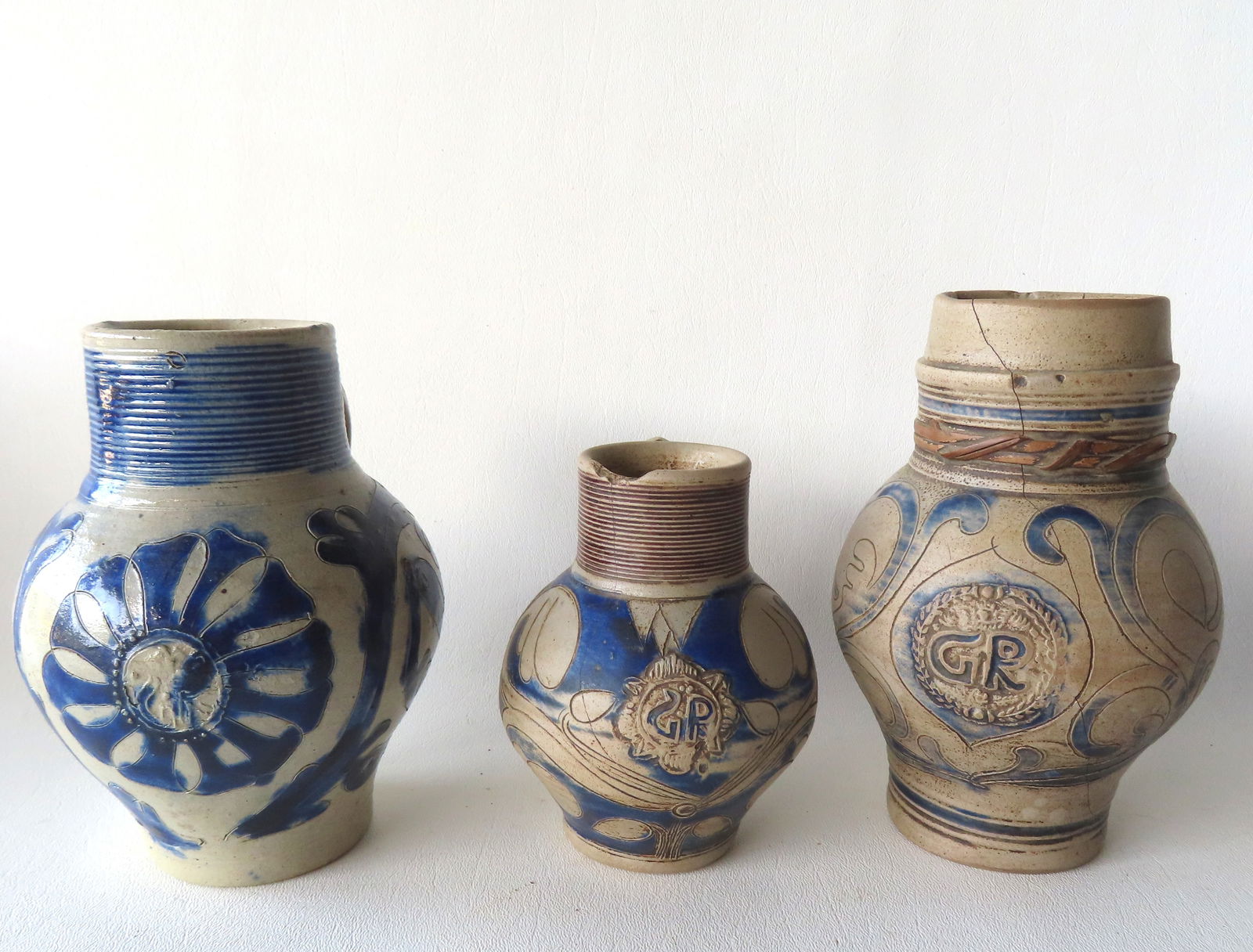 Three Westerwald small bulbous stoneware tankards, all lacking lids, 18th/19th century. The first: Three Westerwald small bulbous stoneware tankards, all lacking lids, 18th/19th century. The first with an incised floral medallion on the front flanked by incised scrolled flowers all brushed in cobal
