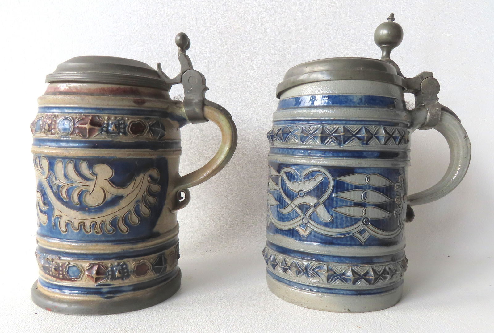Two Westerwald cylindrical tankards with pewter lids, 18th century. The first with 2 narrow bands: Two Westerwald cylindrical tankards with pewter lids, 18th century. The first with 2 narrow bands decorated with various small raised ornaments including geometric shapes and lion's head masks, all wa