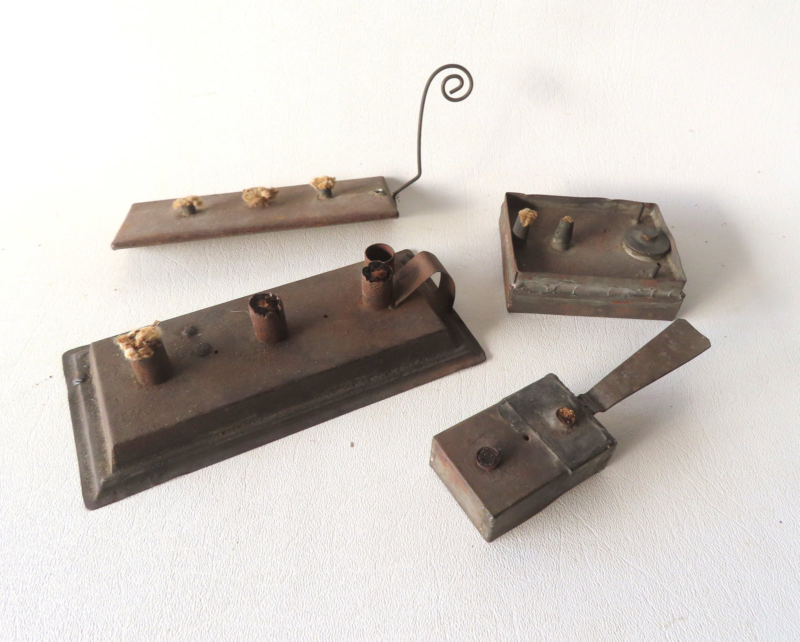 Four early miniature tin fat burning lamps, 18th/19th century. The one in rectangular shape with the: Four early miniature tin fat burning lamps, 18th/19th century. The one in rectangular shape with the scrolled tail like handle is missing the refill cap, else good condition; the others with use wear 