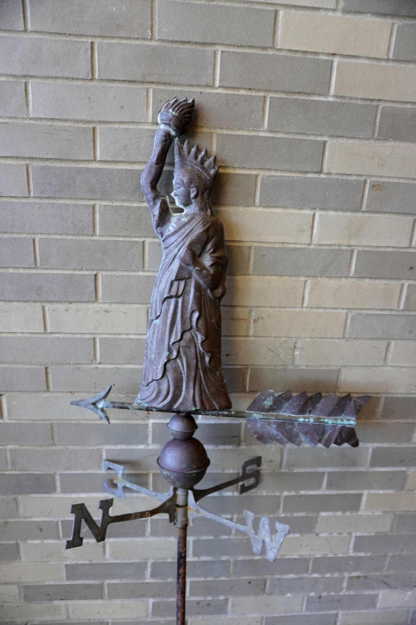A Statue of Liberty copper weathervane, late 20th century, mounted on arrow and with directionals.: A Statue of Liberty copper weathervane, late 20th century, mounted on arrow and with directionals. Note that the weathervane came loose from the arrow and has been reattached with copper wire. Total s