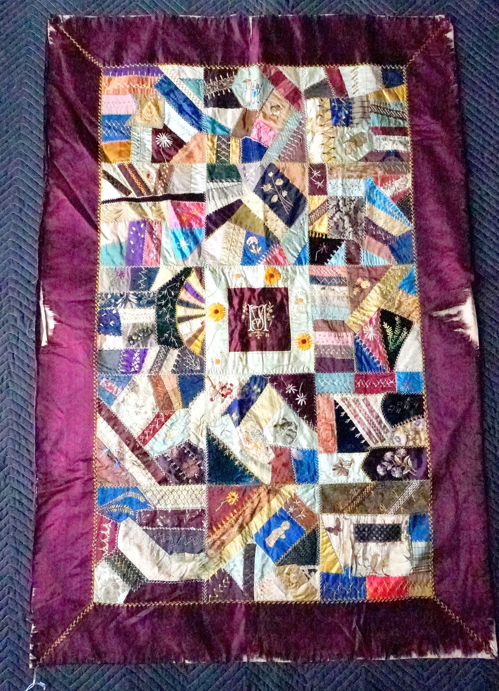 A youth size silk crazy quilt with maroon velvet backing dated 1880.: A youth size silk crazy quilt with maroon velvet backing - decorated with flowers, young girl wearing bonnet, man and woman, 2 kittens, etc. Embroidered initials in center along with date 1880. The si