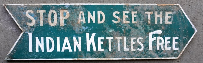 A double sided wooden arrow shaped sign marked "STOP AND SEE THE INDIAN KETTLES / FREE" in original