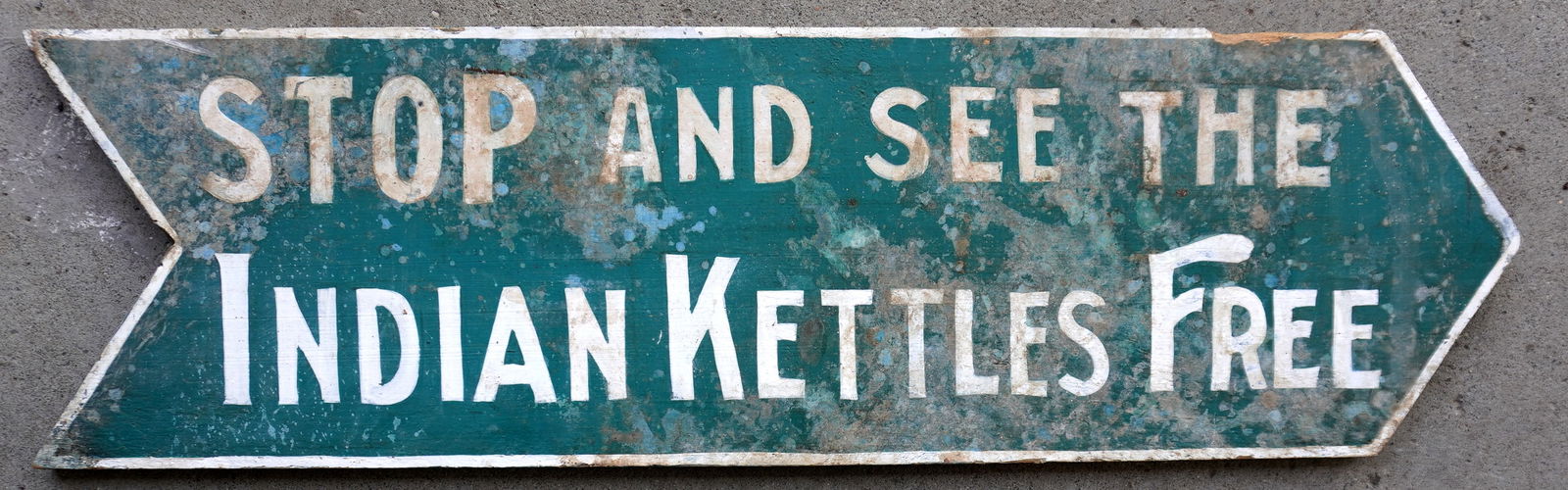 A double sided wooden arrow shaped sign marked "STOP AND SEE THE INDIAN KETTLES / FREE" in original: A double sided wooden arrow shaped sign marked "STOP AND SEE THE INDIAN KETTLES / FREE" in original green and white paint. Needs cleaning otherwise very good condition. Measures 40"L x 11 1/2"H. Note