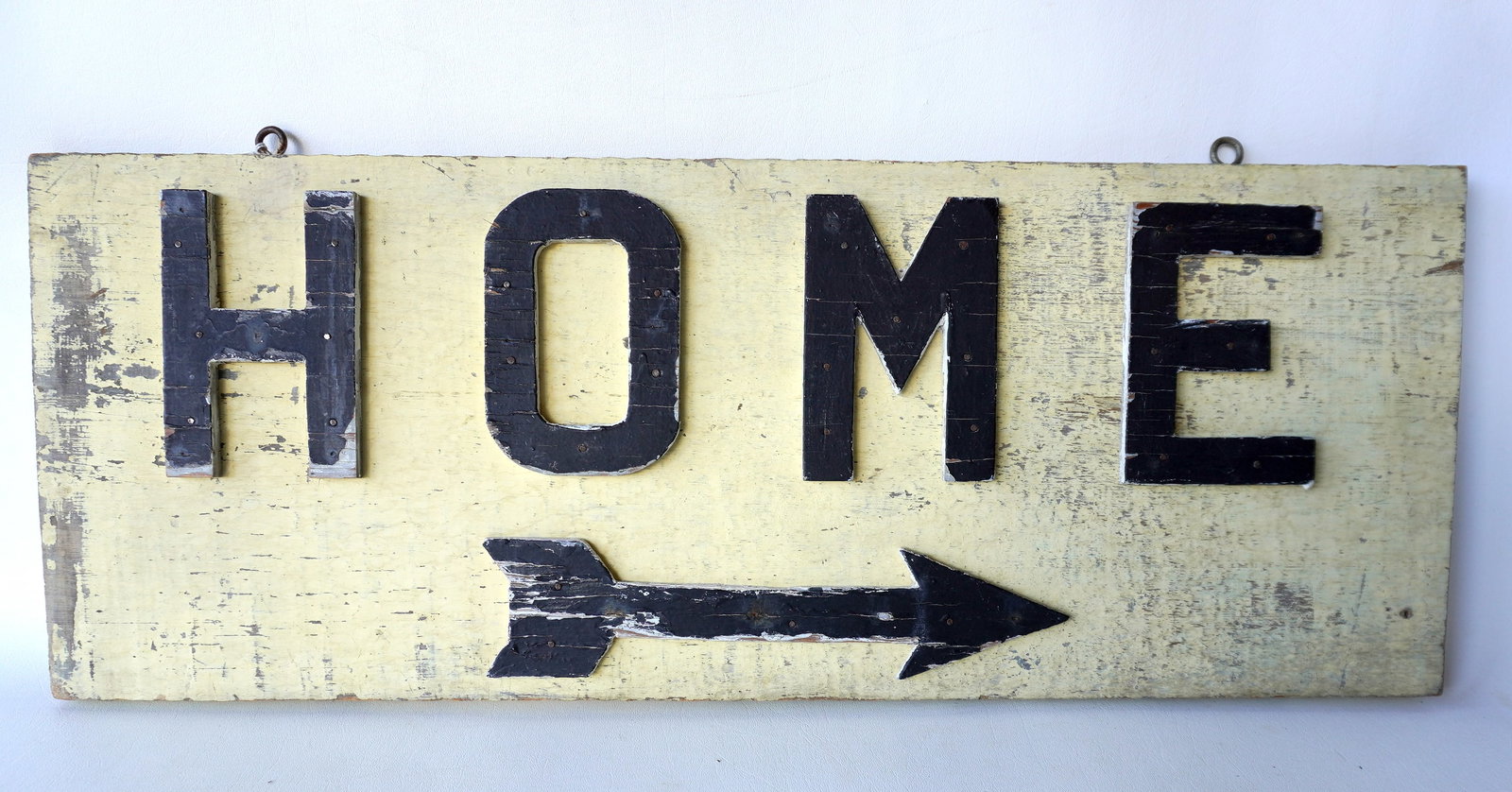 A vintage wooden sign with applied wood letters marked "HOME" with painted directional arrow,: A vintage wooden sign with applied wood letters marked "HOME" with painted directional arrow, lettering black on light yellow, circa 1950. Some paint wear and losses overall good condition. Measures 3