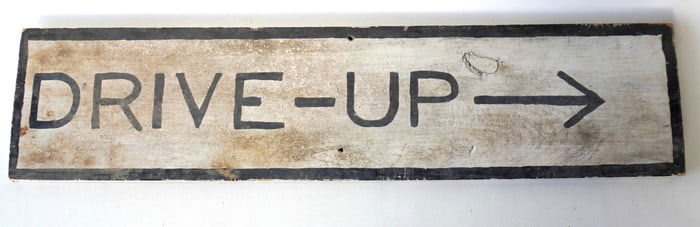 A wooden sign, with primitive hand painting marked "DRIVE-UP" with painted directional arrow, circa