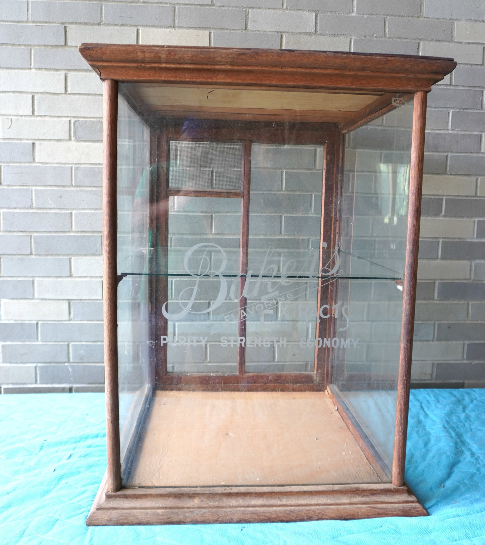 An advertising country store table top rectangular shaped showcase with oak frame having a molded: An advertising country store table top rectangular shaped showcase with oak frame having a molded cornice and base, with etched name in glass front marked "Baker's Flavoring Extract / Purity, Strength