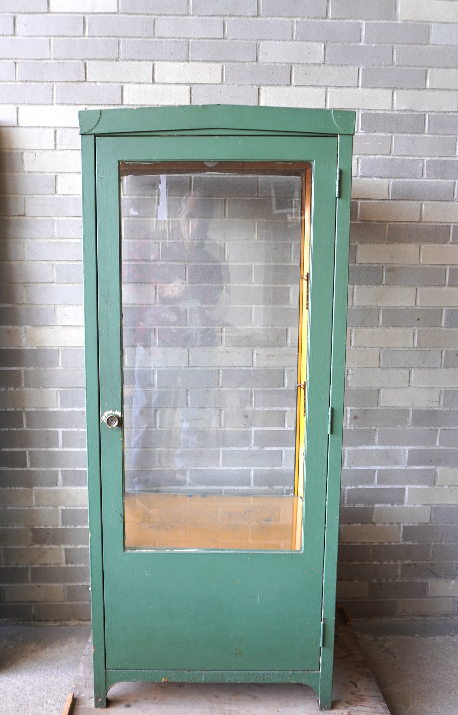 A tall sheet iron medical cabinet with 1 long glass door and glass sides with a pitched roof and 2: A tall sheet iron medical cabinet with 1 long glass door and glass sides with a pitched roof and 2 thick glass shelves - newer green paint and in very good condition, circa 1920. Measures 24 1/4"W x 1