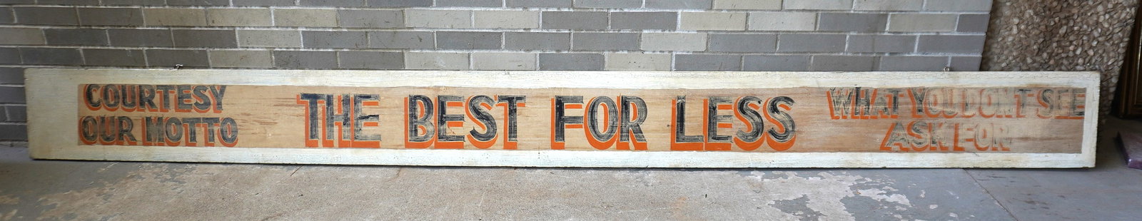 A very long wooden country store building sign in original paint with blue and orange shadow: A very long wooden country store building sign in original paint with blue and orange shadow lettering on cream colored ground that reads in 3 sections "COURTESY OUR MOTTO / THE BEST FOR LESS / WHAT Y