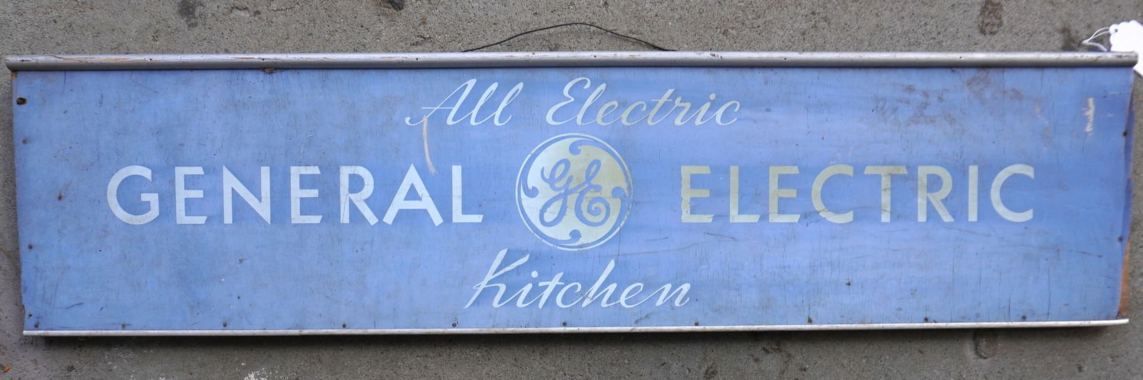 Wooden signed marked "All Electric GENERAL ELECTRIC Kitchen", white lettering on a blue ground -: Wooden signed marked "All Electric GENERAL ELECTRIC Kitchen", white lettering on a blue ground - metal frame but missing side moldings, overall good condition, circa 1960". Measures 48" x 12". Provena