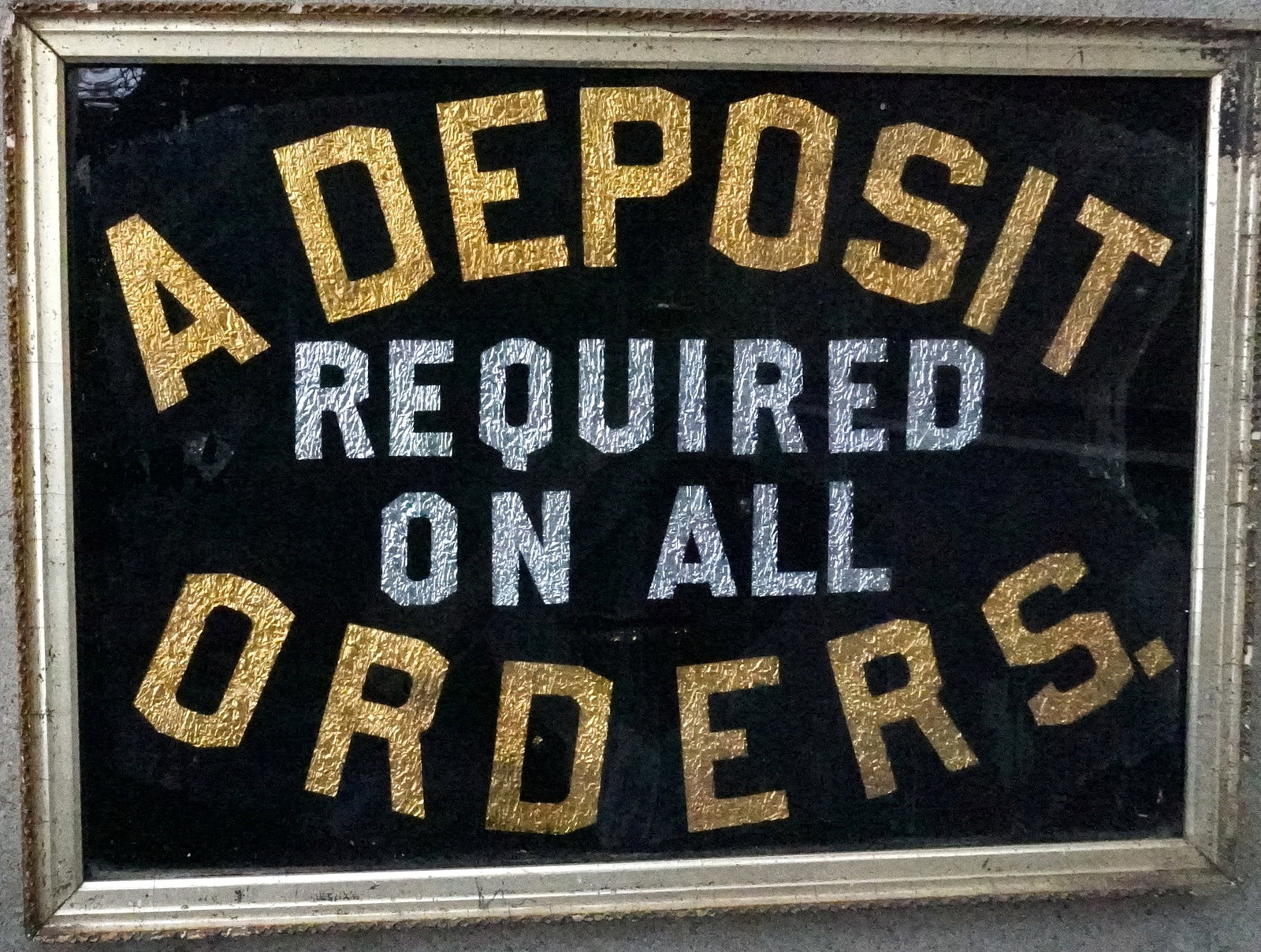 A tinsel advertising sign, gold and silver lettering on painted black ground, marked "A DEPOSIT: A tinsel advertising sign, gold and silver lettering on painted black ground, marked "A DEPOSIT REQUIRED ON ALL ORDERS", housed in original frame, late 19th century, good condition. Measures 21 1/2" x