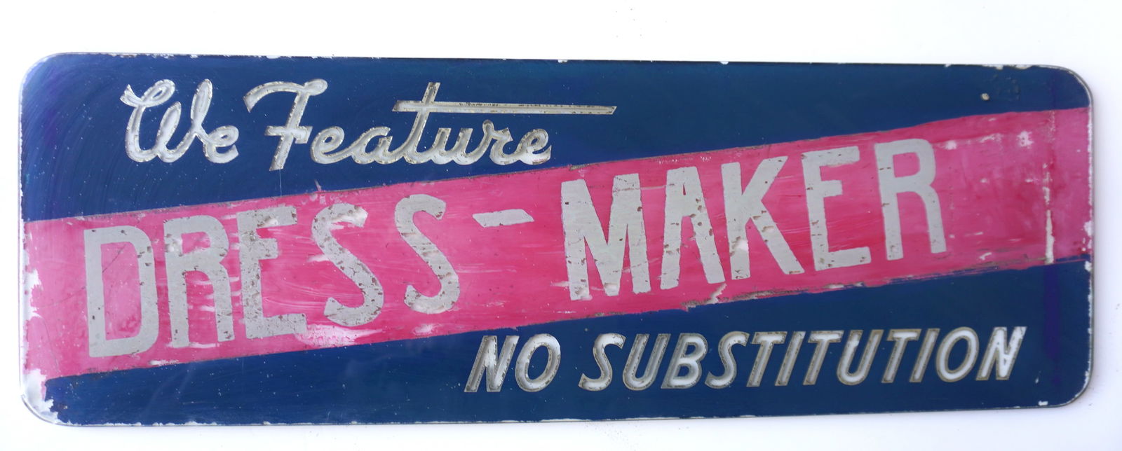 A reverse painted glass sign marked "We Feature / DRESS - MAKER / No Substitution". Some paint wear,: A reverse painted glass sign marked "We Feature / DRESS - MAKER / No Substitution". Some paint wear, and overall fair to good condition, circa 1930-50. Measures 24"W x 8"H. Provenance: From the Marni