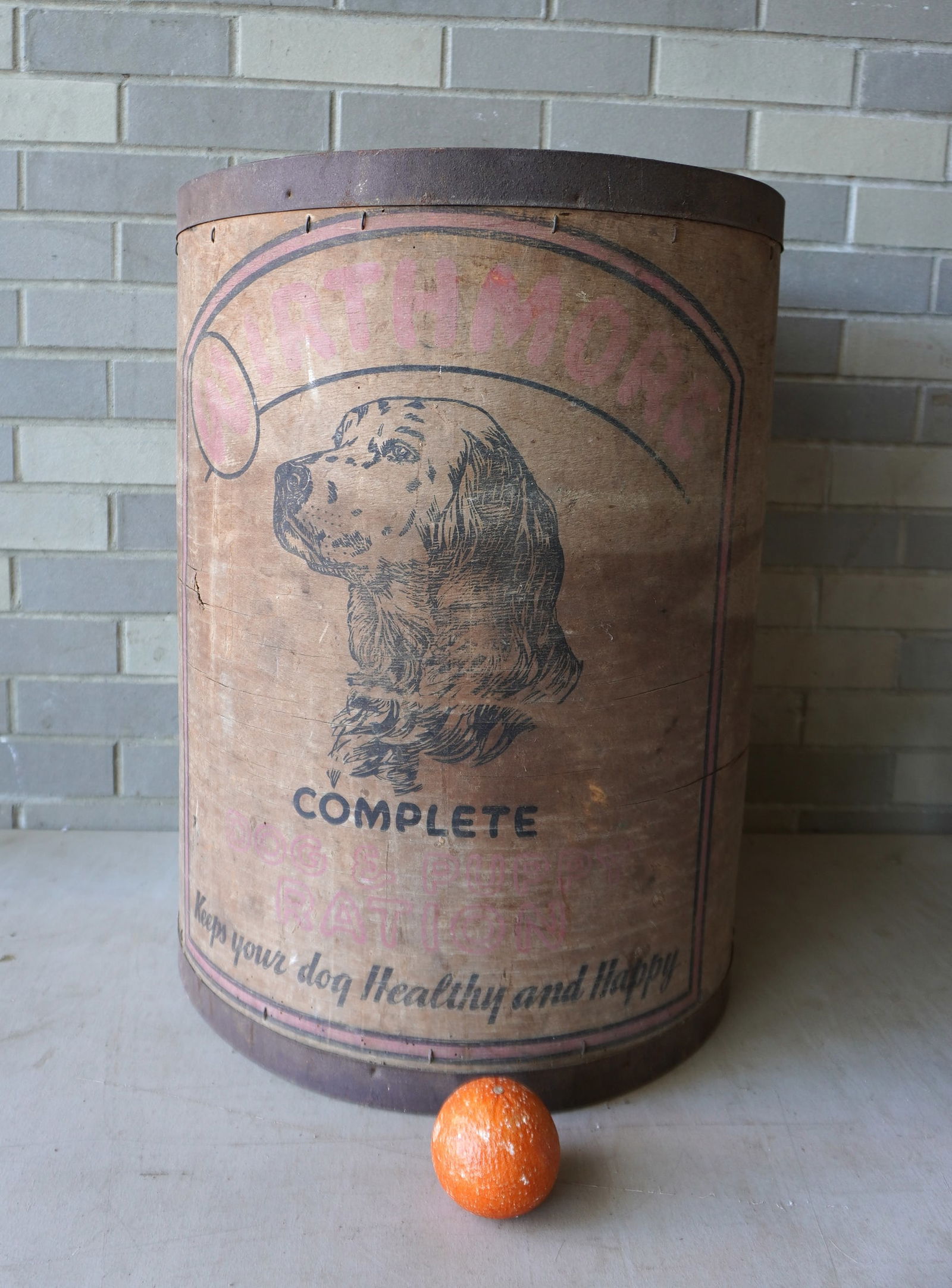 A large cylindrical dog grain bin having a lithograph of a dog on the front side signed "WORTHMORE /: A large cylindrical dog grain bin having a lithograph of a dog on the front side signed "WORTHMORE / COMPLETE DOG & PUPPY RATION" - the paint is faded and the paper covering the wooden bottom is worn,