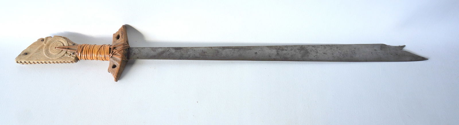A Philippine Kampilan heavy duty combat sword that appears to have a carved whale bone figural: A Philippine Kampilan heavy duty combat sword that appears to have a carved whale bone figural pommel, woven rattan grip, carved wooden hand guard, and a spikelet at end of the blade, 19th century. Co