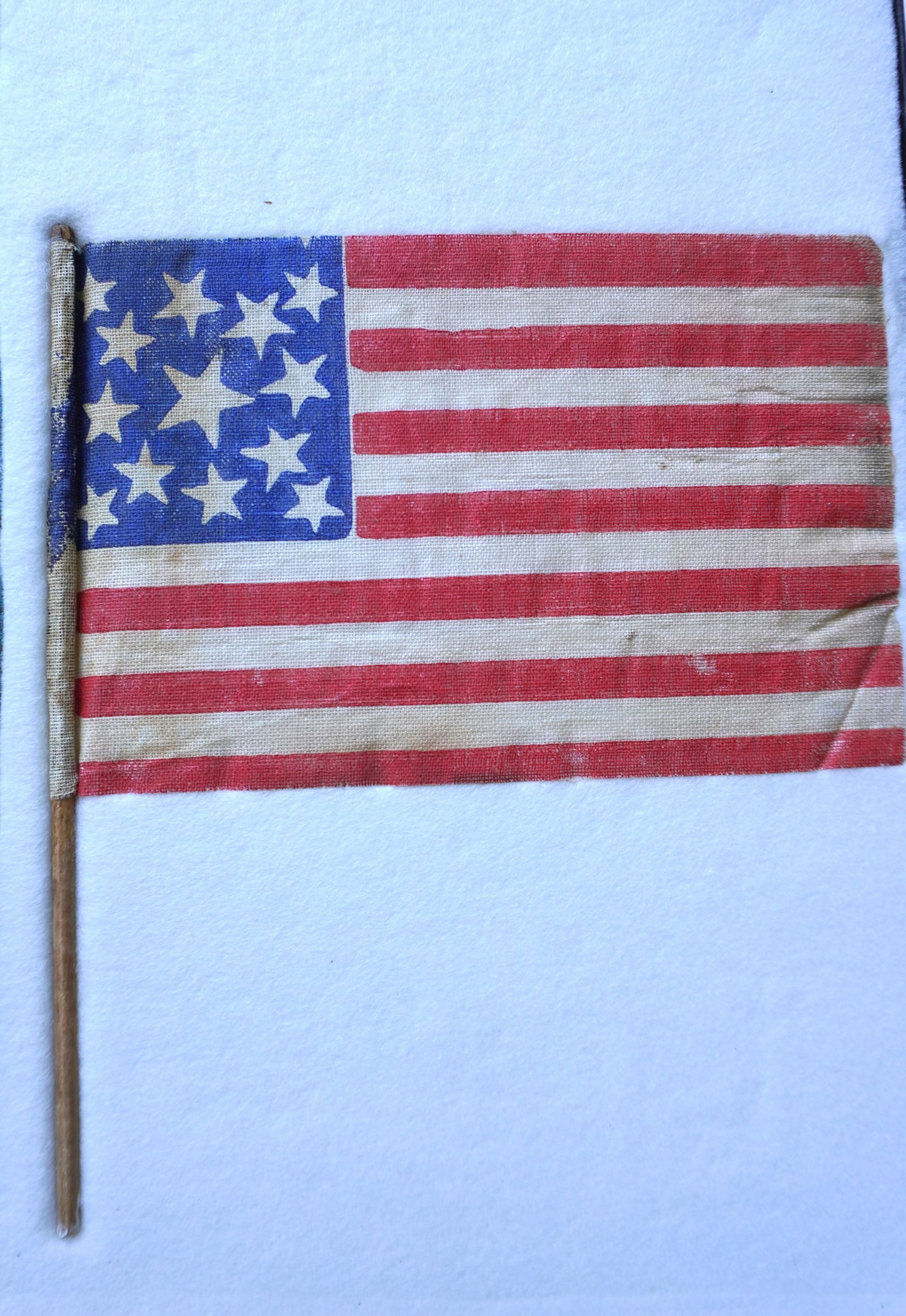 An American Centennial 13 star parade flag attached to original wooden post. Slight wear to the red: An American Centennial 13 star parade flag attached to original wooden post. Slight wear to the red stripes, hardly noticeable, else very good condition. The flag measures 7" x 4 1/2". Note attached i