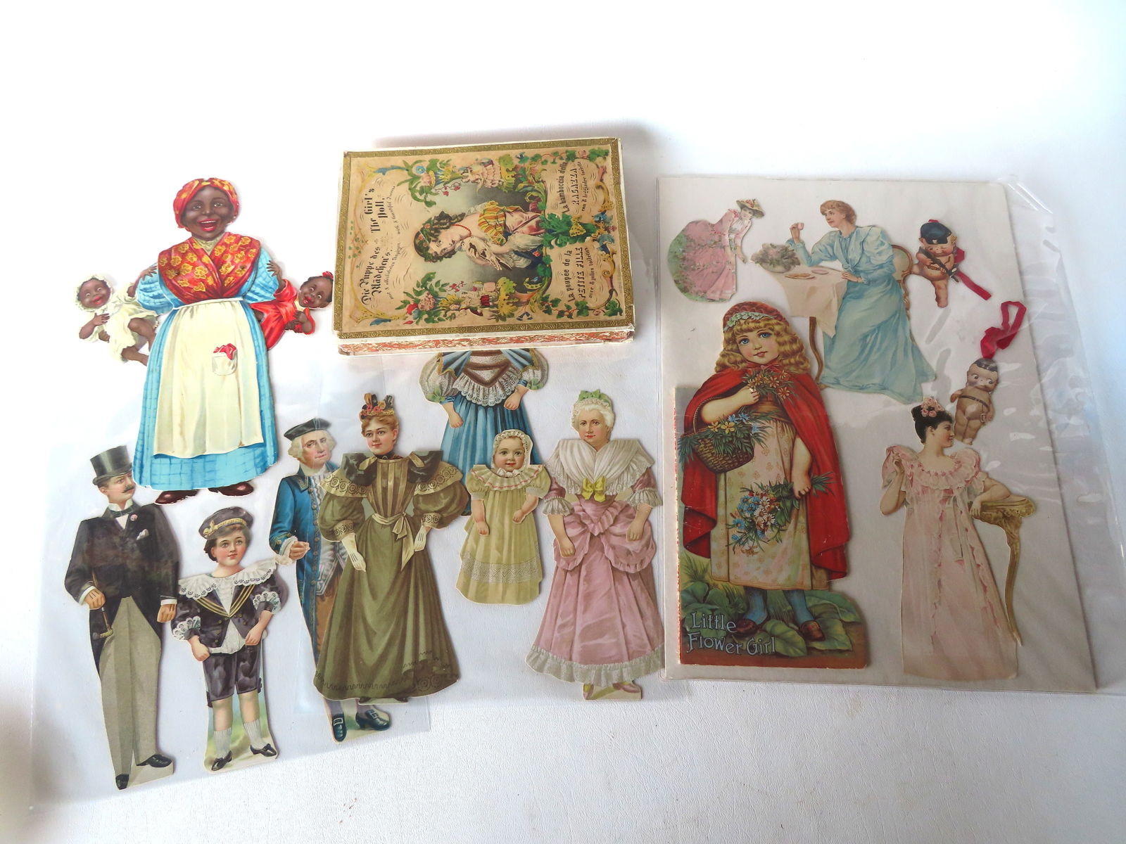 Grouping of 19th century die cuts, doll cutouts, etc., including: A Raphael Tuck mechanical die-cut: Grouping of 19th century die cuts, doll cutouts, etc., including: A Raphael Tuck mechanical die-cut of lady holding 2 babies titled "Dinah and her 'Darlings'" with poem on reverse regarding Black & Wh