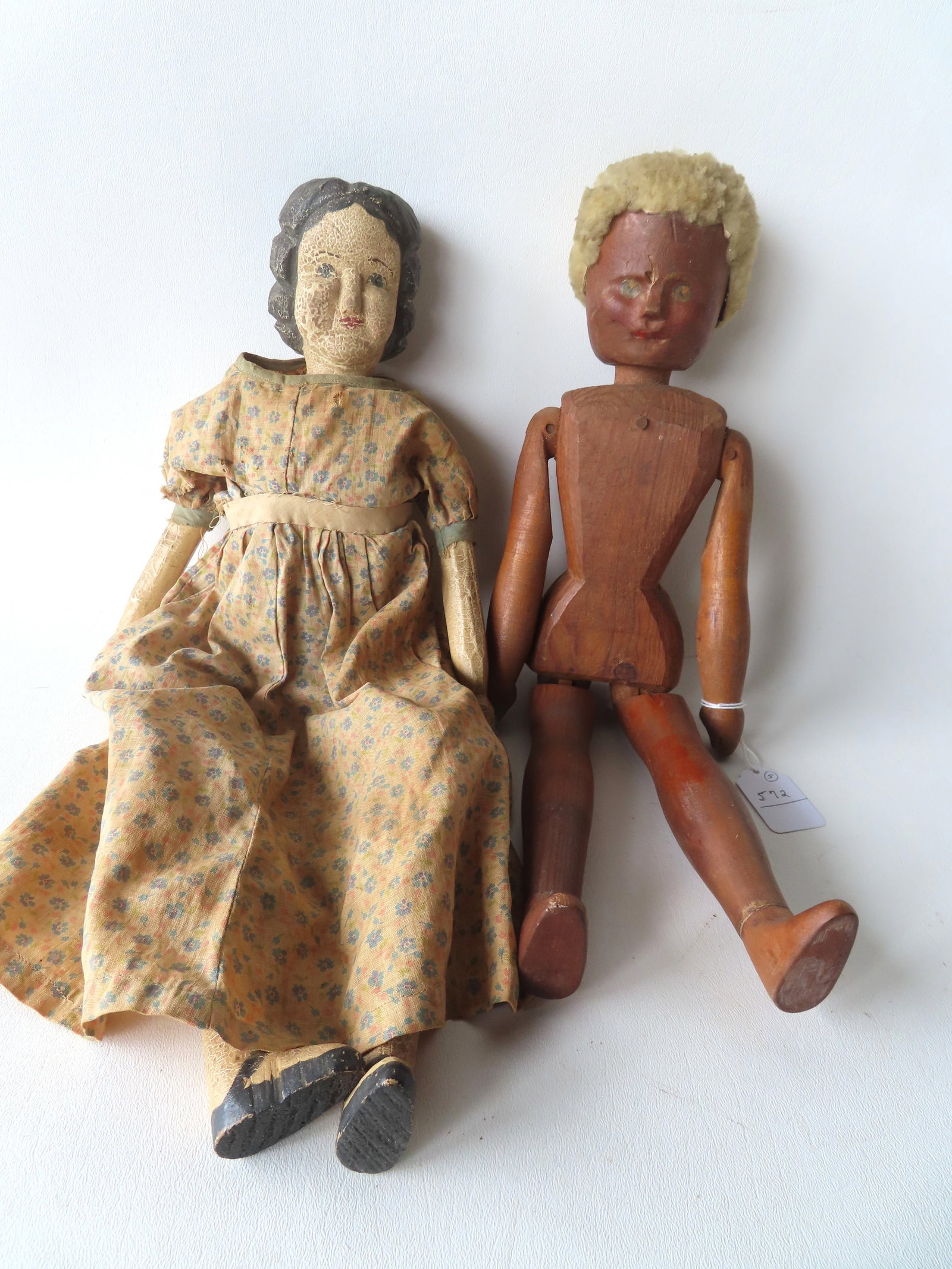 Two folk art hand carved wooden dolls with note of family provenance found with the dolls. The: Two folk art hand carved wooden dolls with note of family provenance found with the dolls. The first, jointed and pegged construction with curled white hair, probably sheep skin, and in original darke