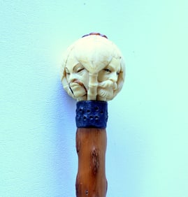 A carved bone 4 face walking stick with tarnished silver collar attached to rustic briarwood shaft