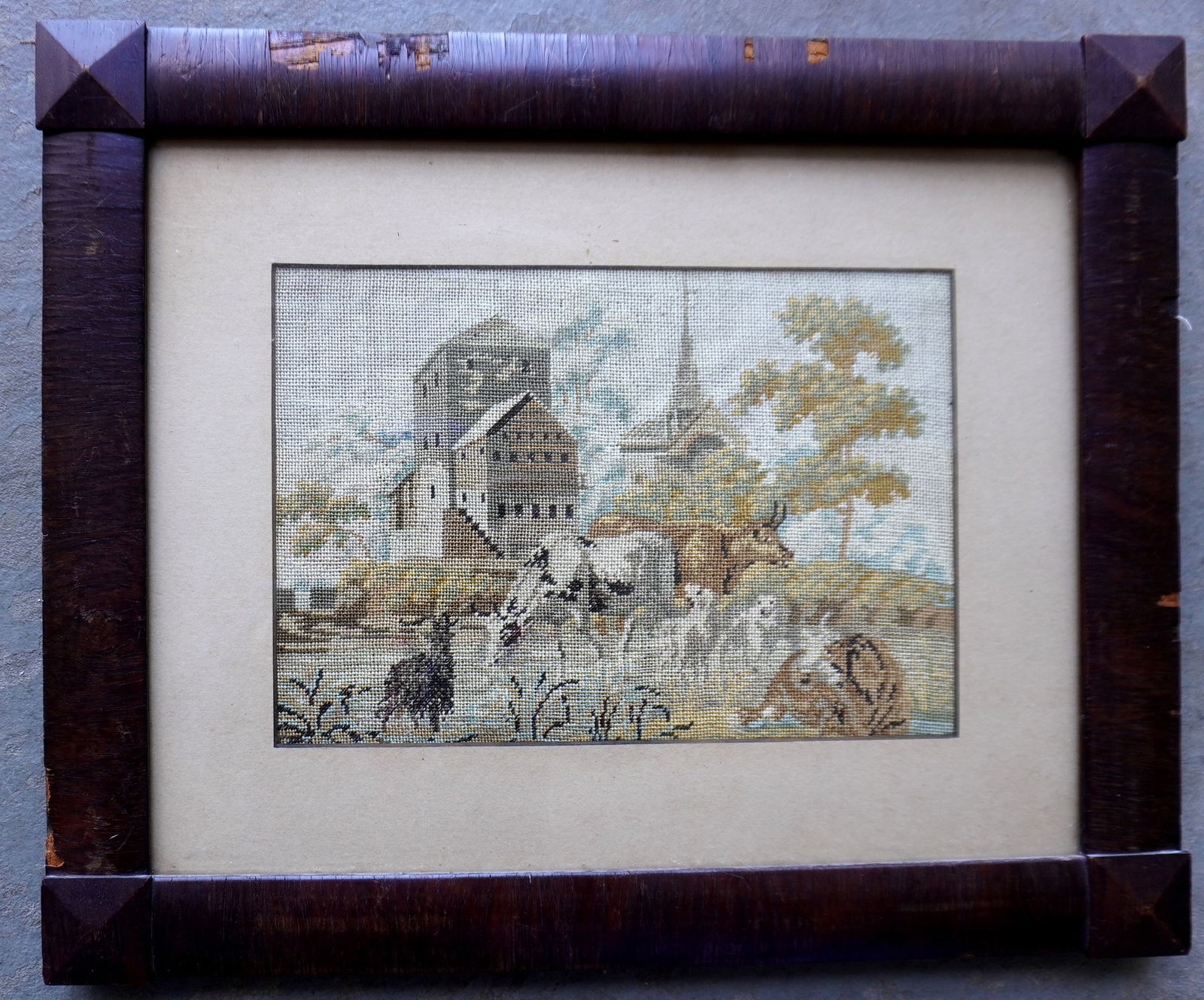 A framed petit point textile depicting cows and sheep feeding in pasture with institutional building: A framed petit point textile depicting cows and sheep feeding in pasture with institutional building and church in background, mid 19th century, and in very good condition. The mahogany frame which ap