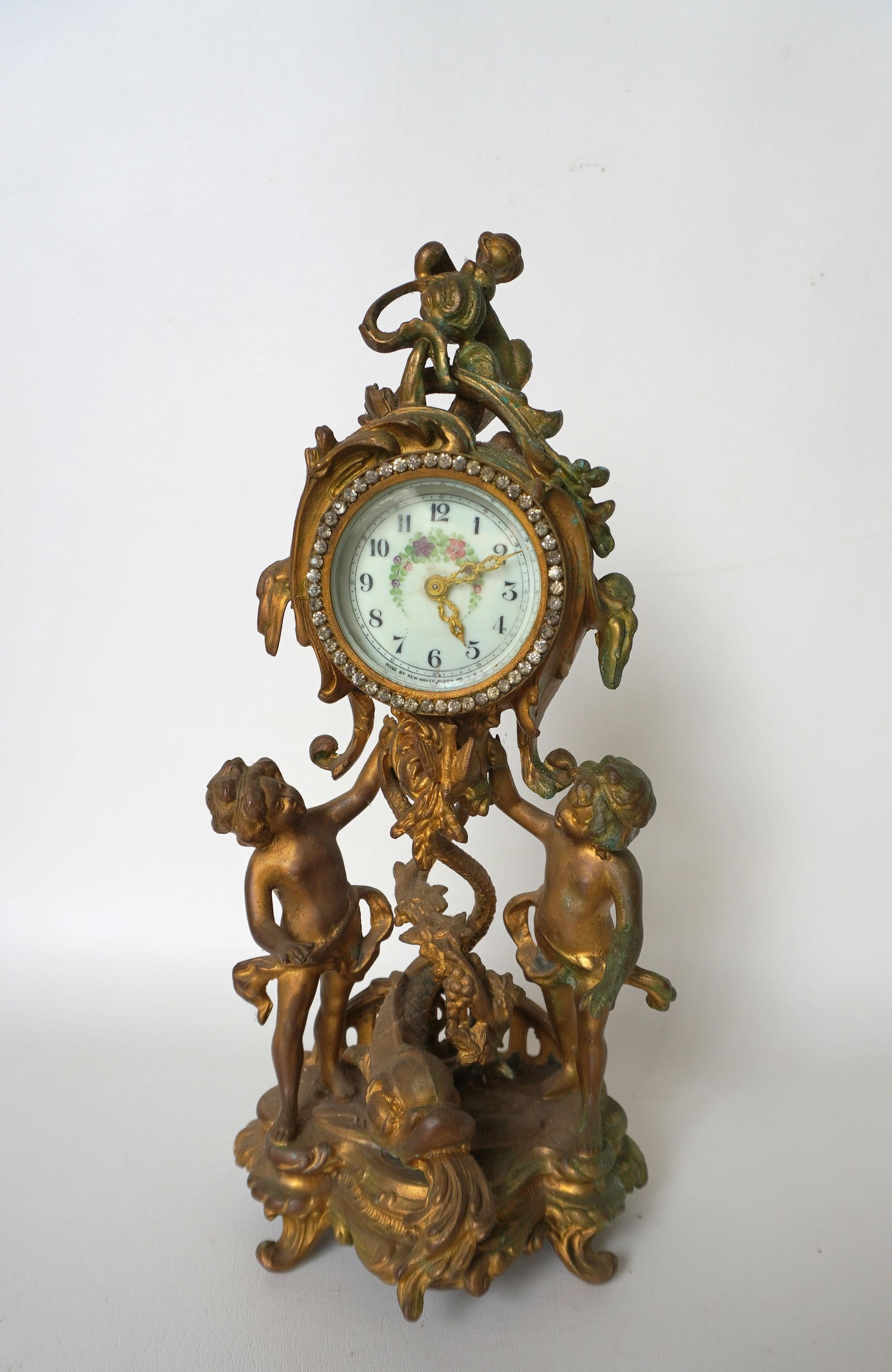 An ornate French style mantle clock decorated with cherubs, dolphin, grapes and vine and having a (1 of 7)