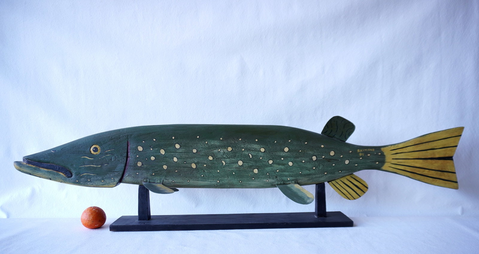 Jeff Raymond, folk art fish carving (1949-2022, Poughkeepsie and Red Hook NY). A large stylized: Jeff Raymond, folk art fish carving (1949-2022, Poughkeepsie and Red Hook NY). A large stylized wooden Pickerel fish carving in original paint with tin fins and mounted on wooden platform - signed on 