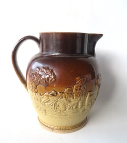 An earthenware water pitcher with brown over yellow glaze depicting a raised hunting scene with
