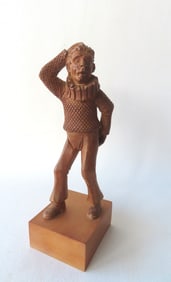 A whimsical carved wooden sculpture of jester scratching his head with one hand and his tush with
