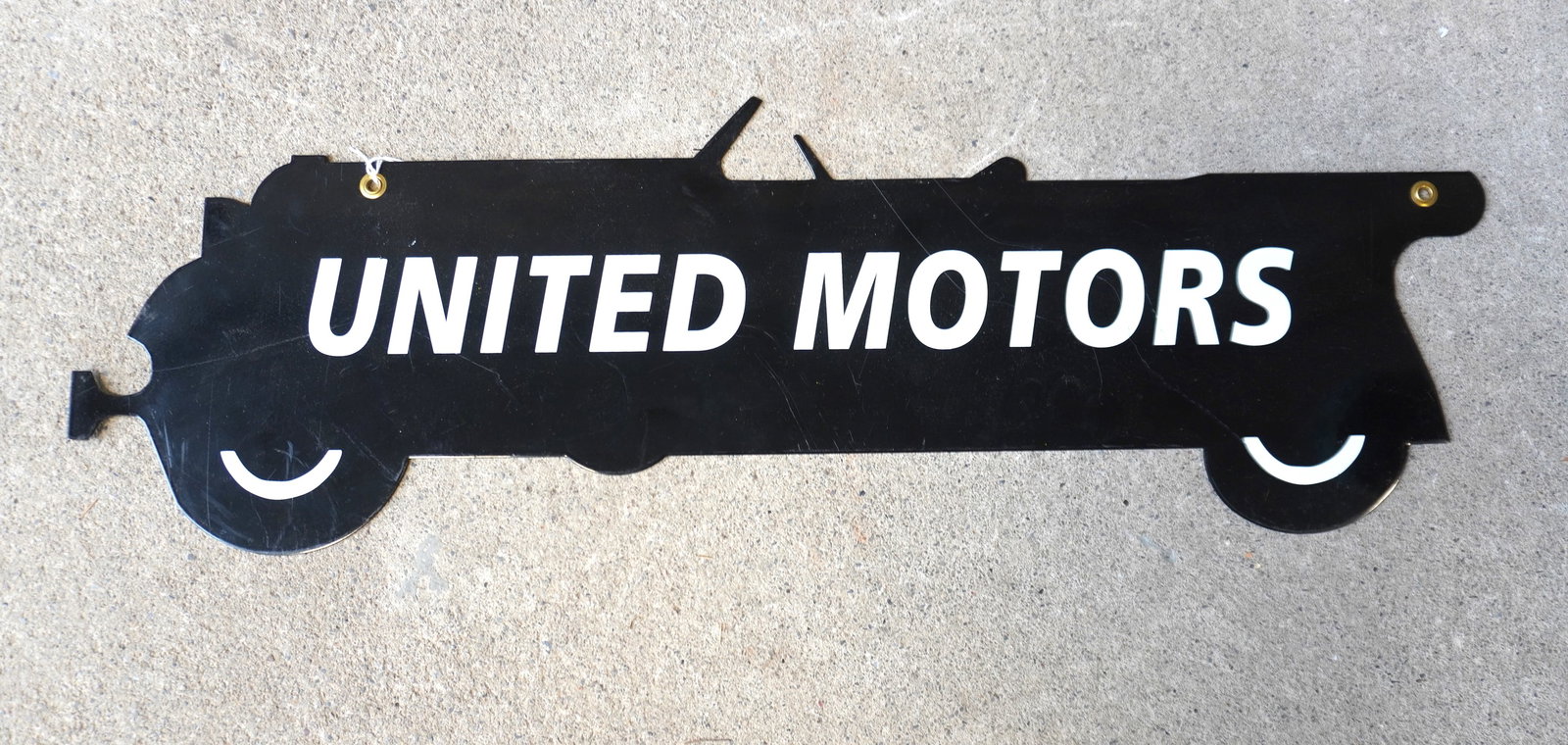 An enameled advertising sign "UNITED MOTORS" in the shape of an open touring car.: An enameled advertising sign "UNITED MOTORS" in the shape of an open touring car - unsure of age. Some surface scratches, otherwise very good condition. Measures 29"L x 9 1/2"L.