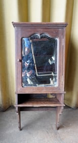 An oak medicine cabinet with shaped beveled mirror door, over a lower attached shelf with shaped
