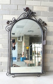 A wrought iron wall mirror with beveled edge. The dome top decorated with wrought iron flowers with